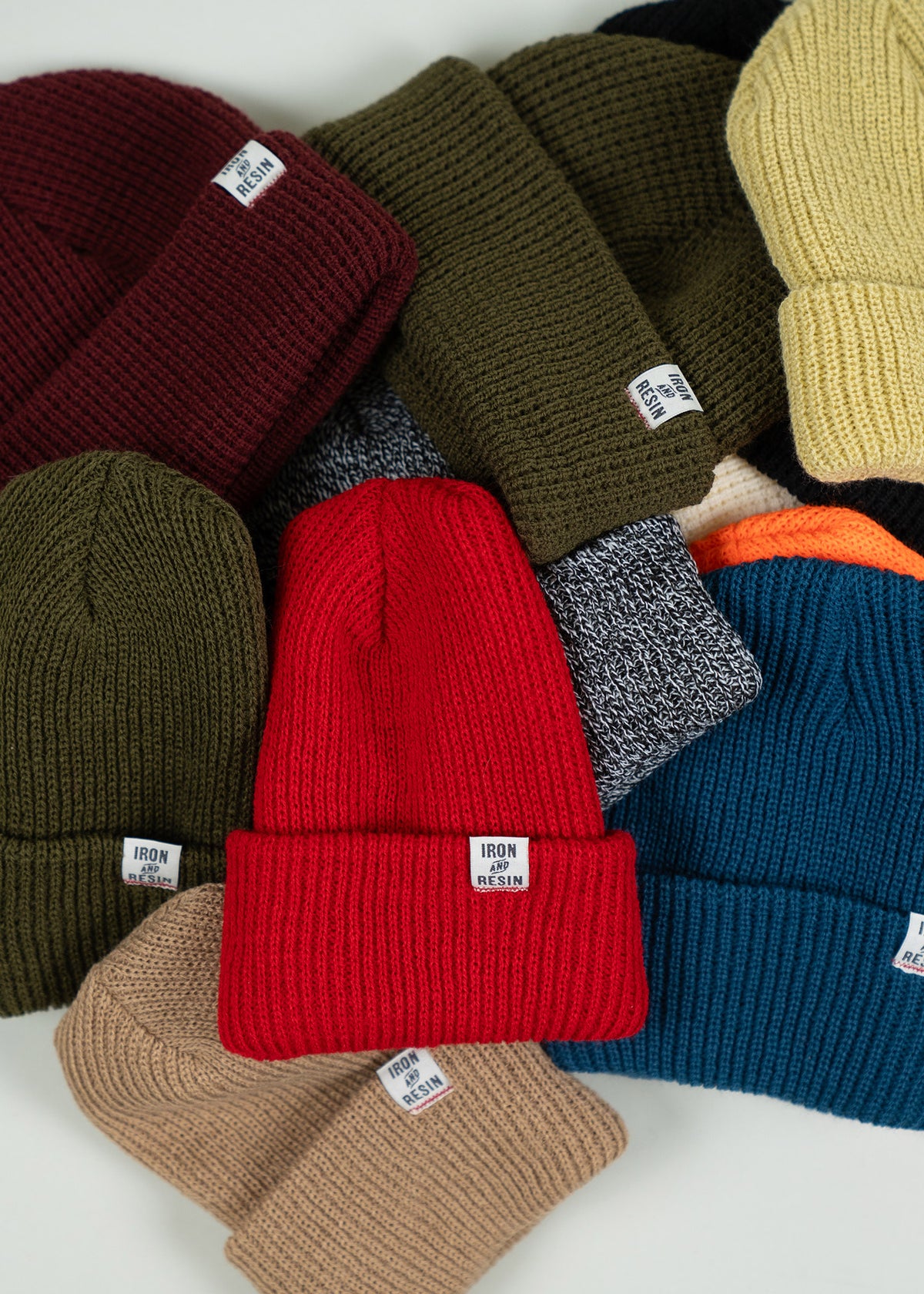 A collection of colorful Iron and Resin beanies, including red, blue, and olive, arranged on a white surface.