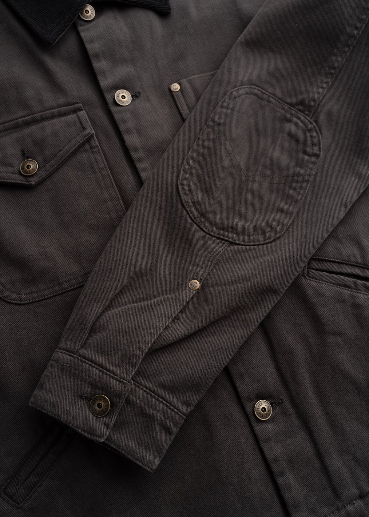 Close up of peach bull denim fabric showing, custom buttons, detailed stitching, custom buttons, textured cotton weave and durable workwear construction