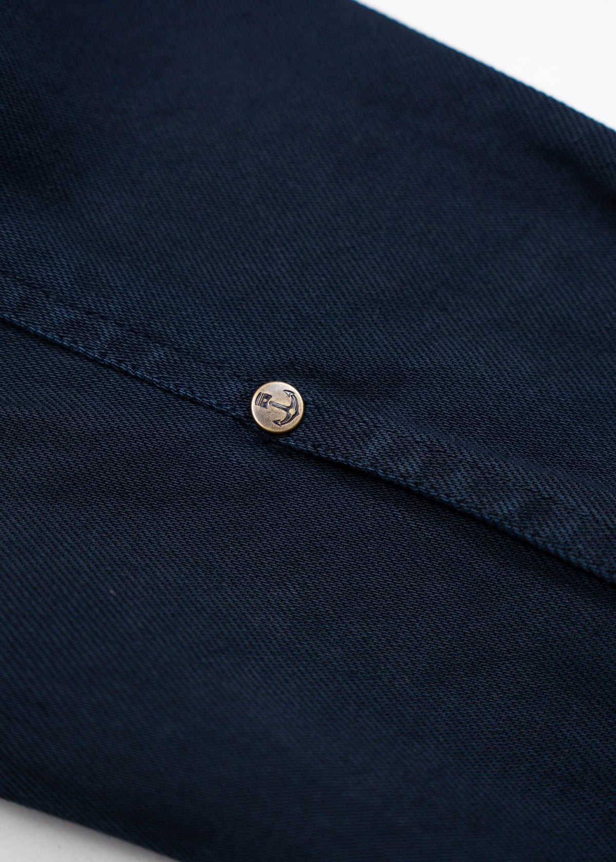 Close-up of a navy blue fabric with a single gold button featuring an anchor design, highlighting texture and detail.
