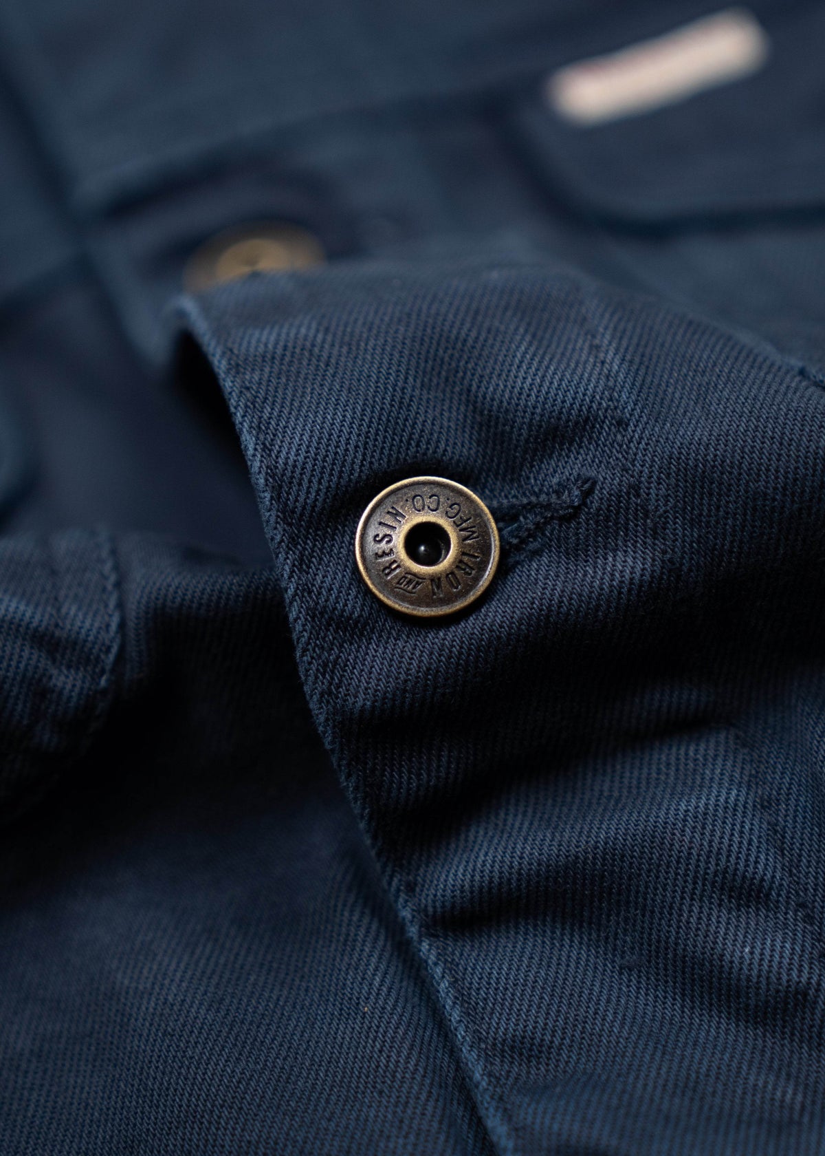 Close-up of a navy blue fabric with a brass snap button, showing texture and detail.