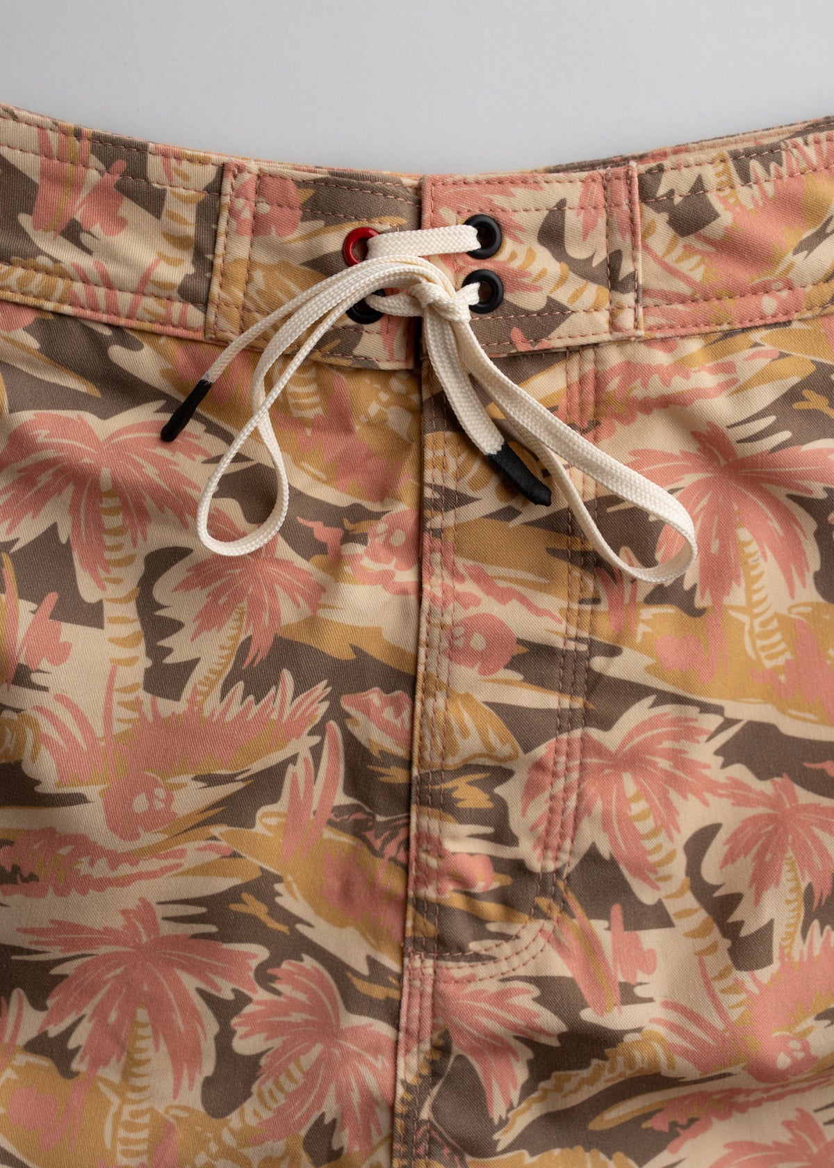 Close-up of tropical-patterned swim trunks with pink and brown palm trees, featuring a white drawstring and black eyelets.