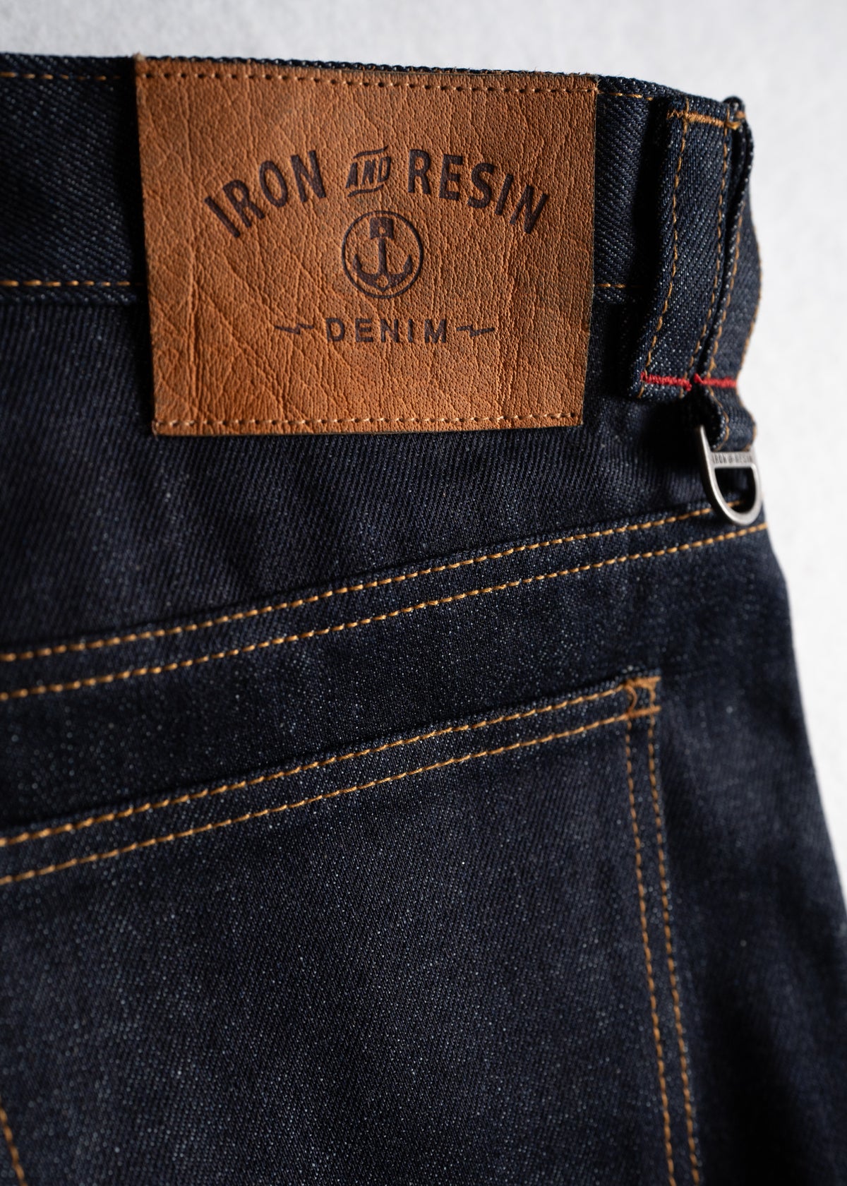 Close-up of Iron and Resin denim jeans with brown leather patch and visible stitching detail on dark blue fabric.