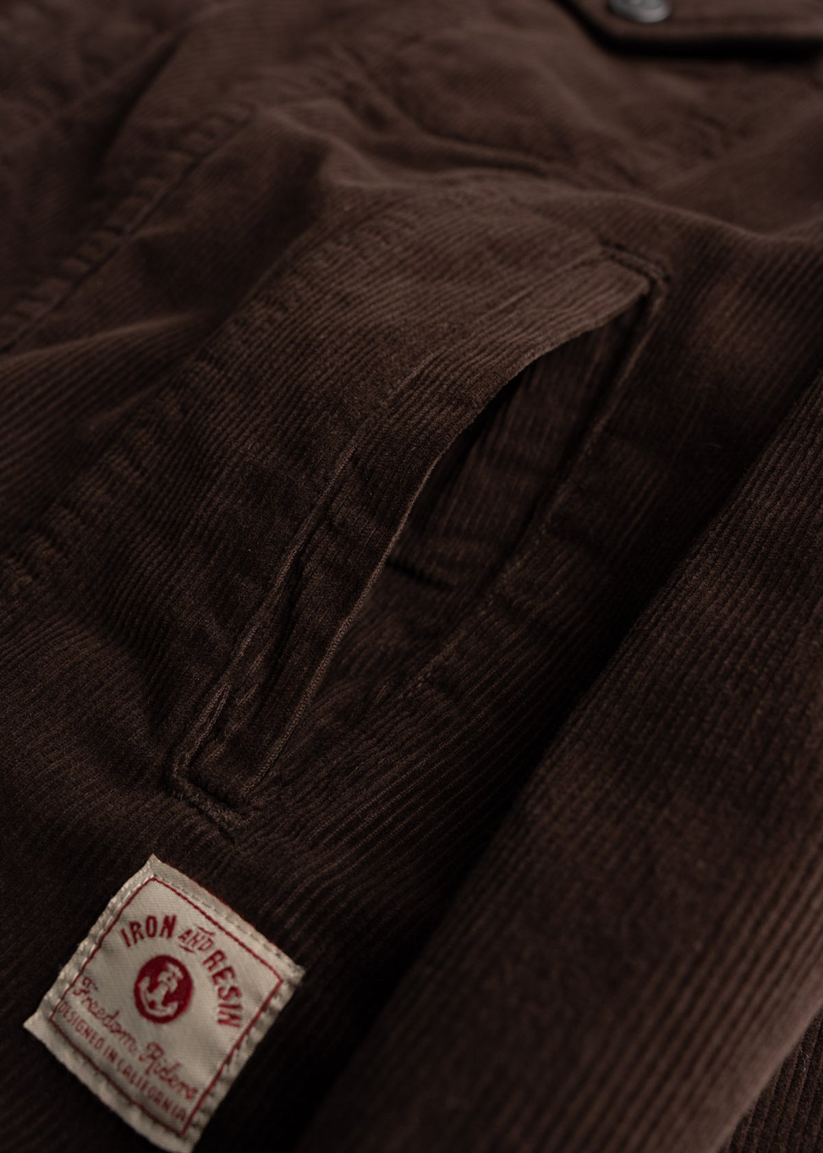 Close-up of a brown corduroy jacket with a visible pocket and an Iron and Resin label at the bottom, highlighting texture.