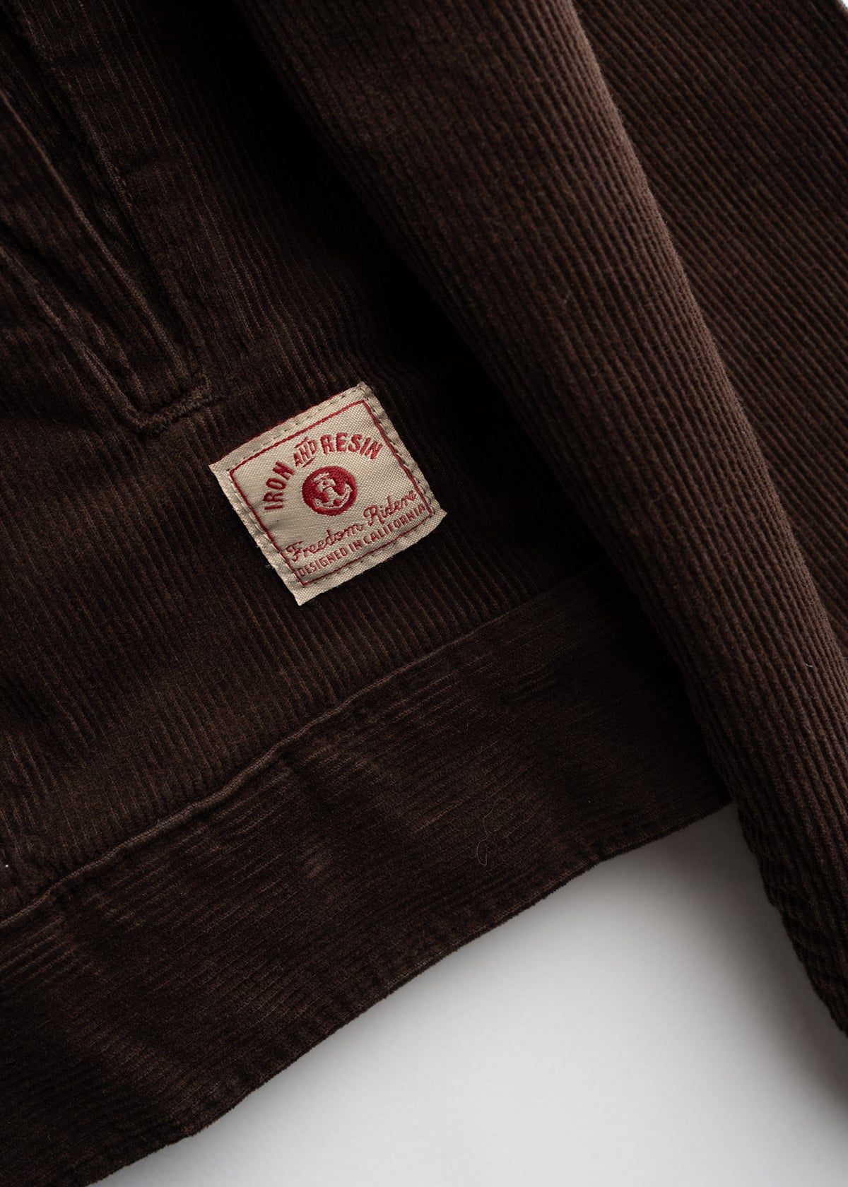 Close-up of a brown corduroy jacket with an Iron and Resin label, highlighting its texture and design details.