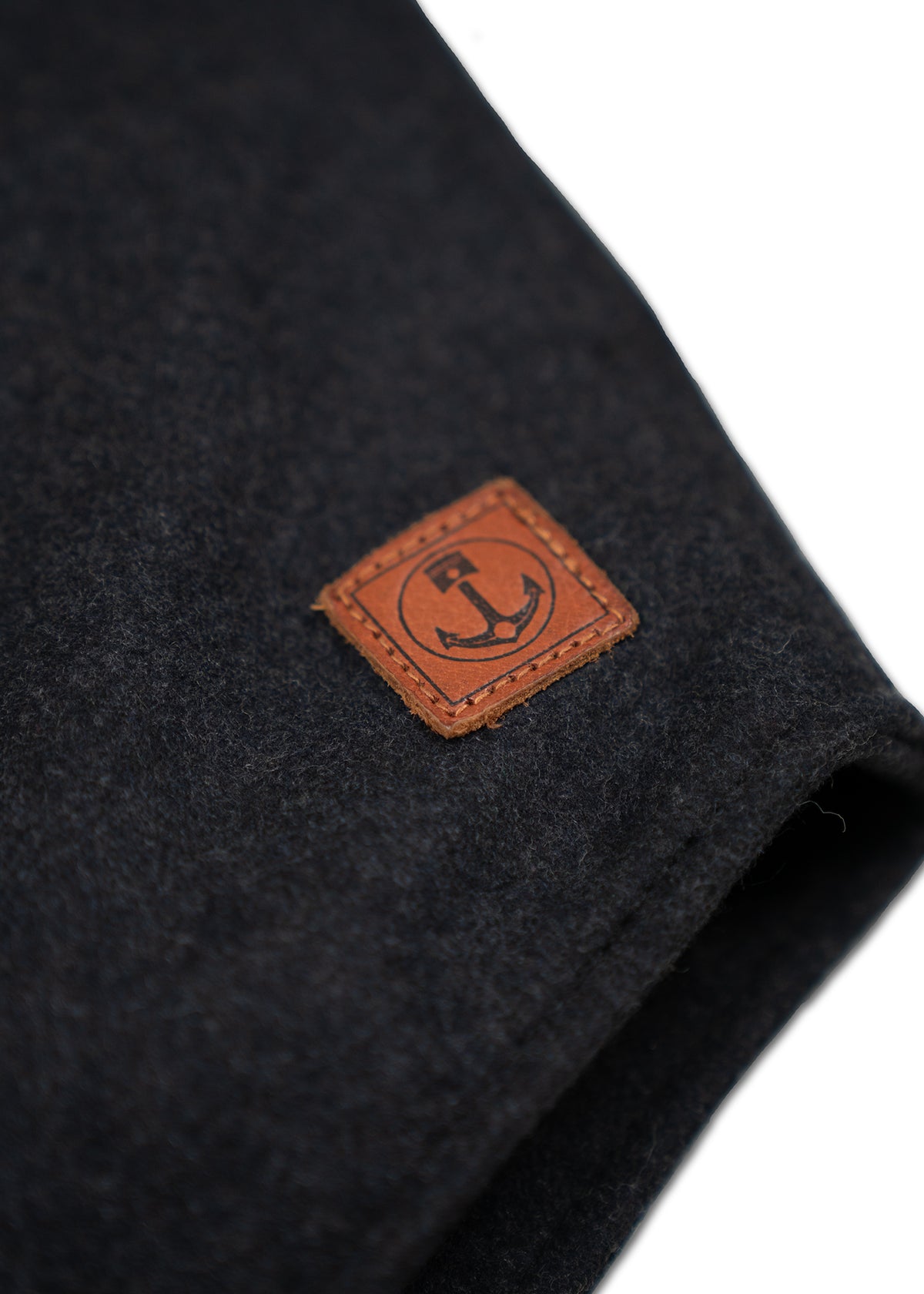 Dark fabric with a brown leather patch featuring an anchor logo, symbolizing nautical style and rugged elegance.