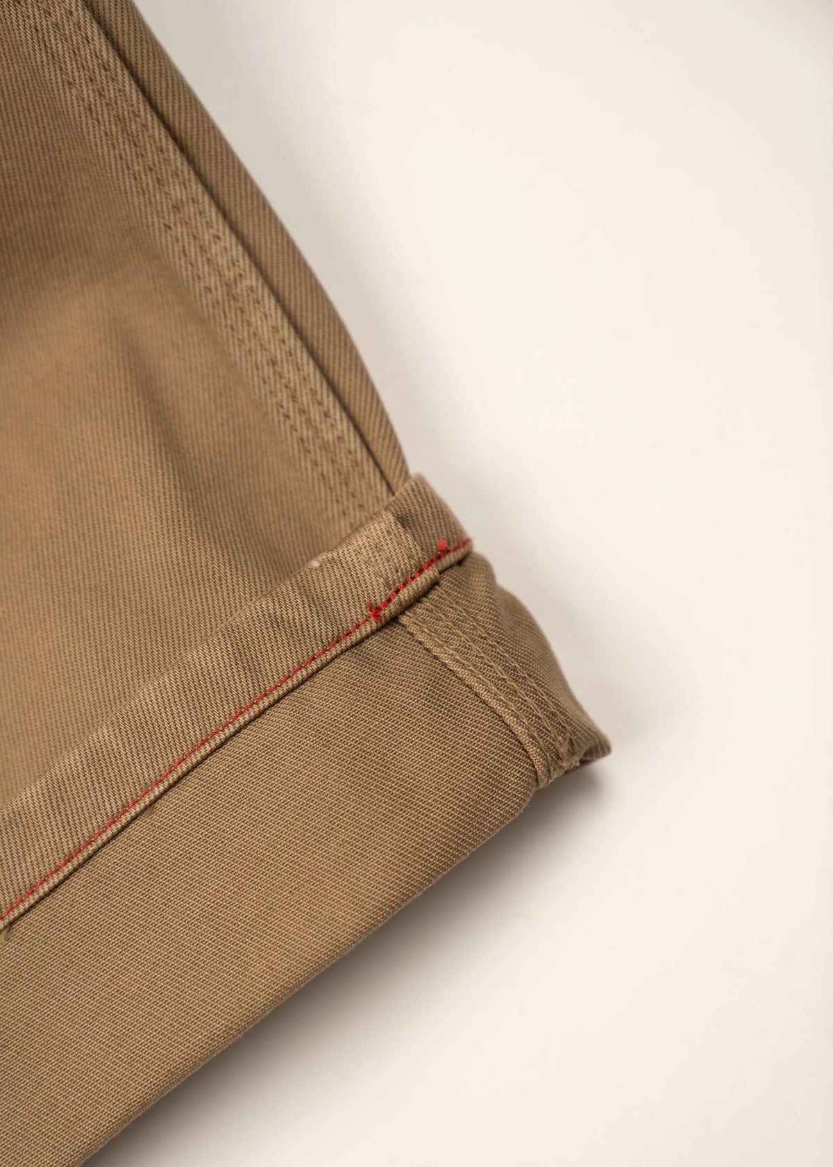 Close-up of khaki fabric with red stitching detail, showcasing the texture and craftsmanship of the material on a light background.