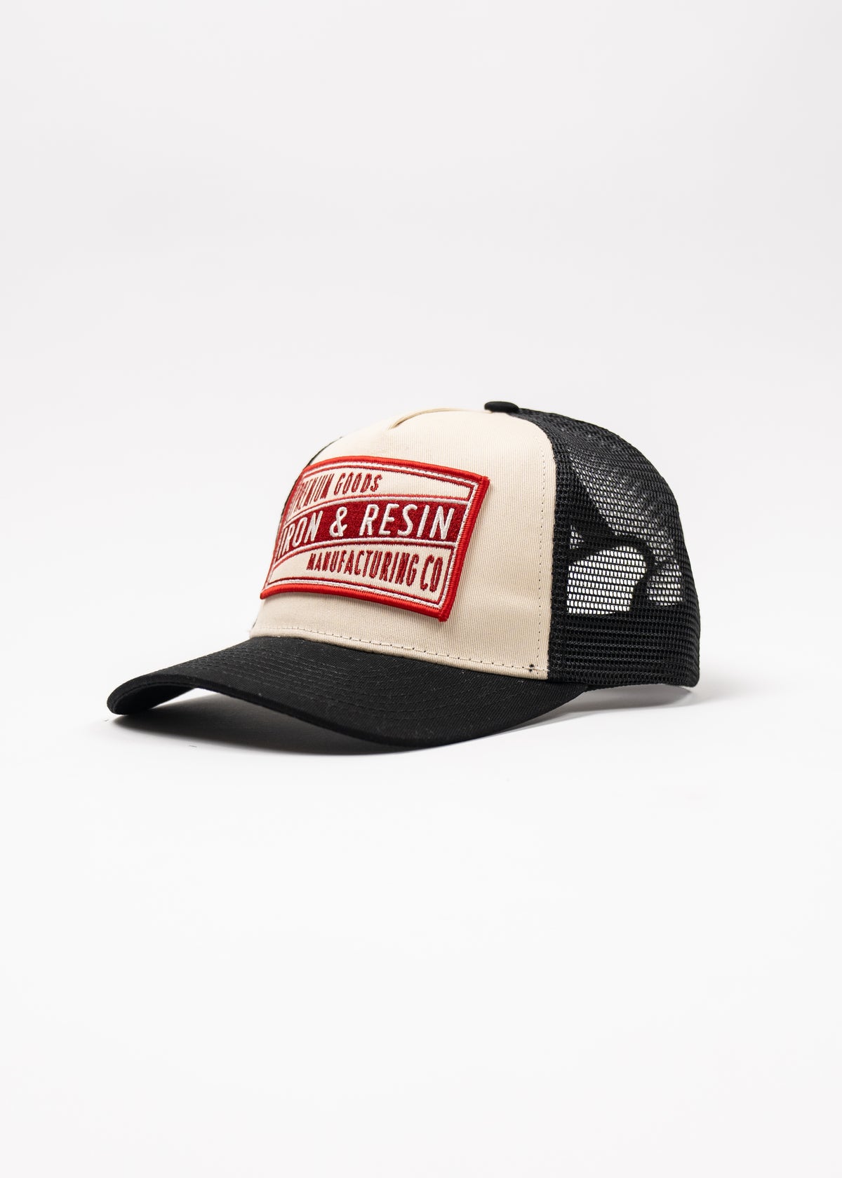 Trucker cap with black mesh, beige front, and red "Iron & Resin Manufacturing Co" patch, set against a white background.