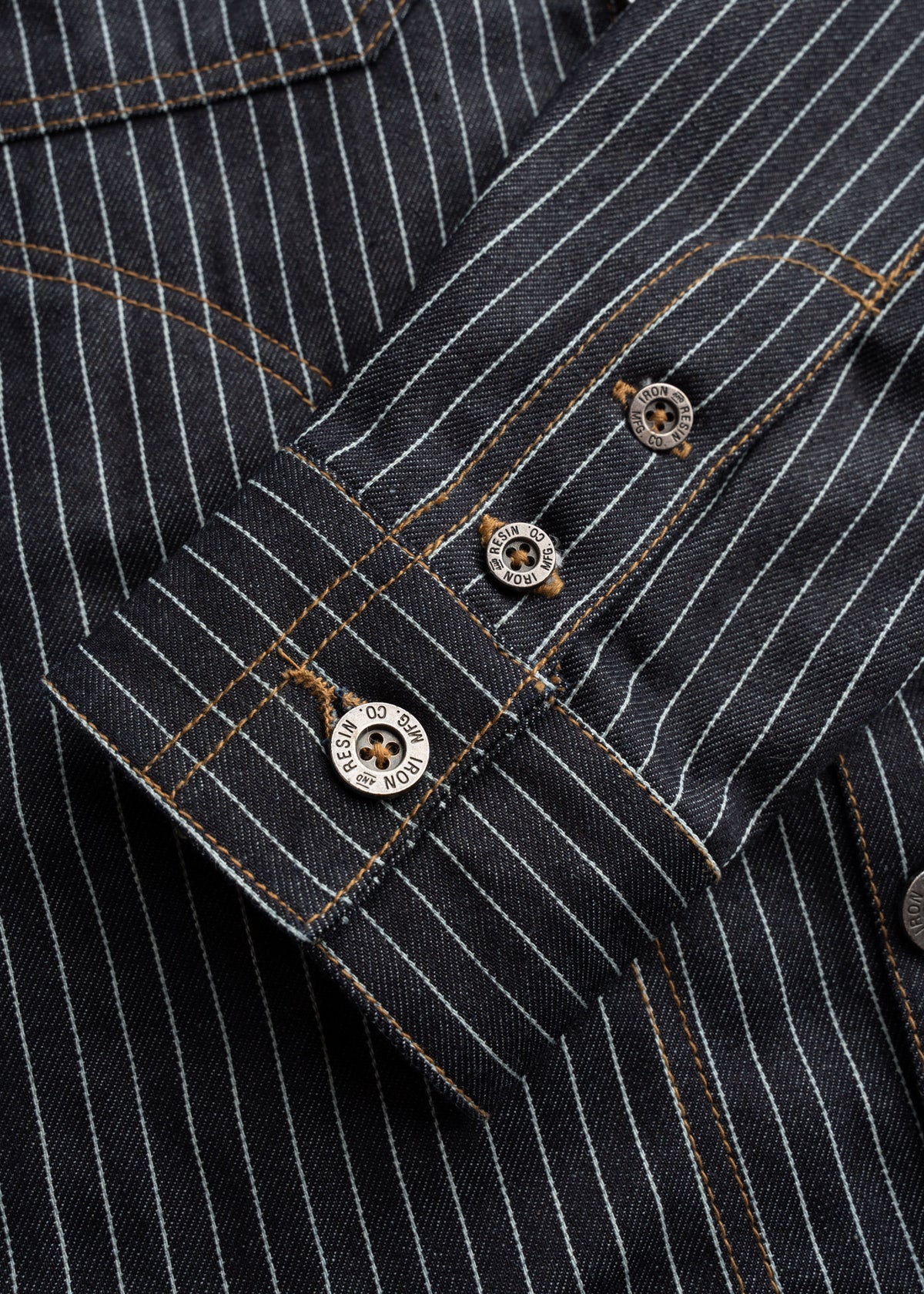 Close up of metal buttons on striped denim shirt, highlighting hardware detail and stitching detail