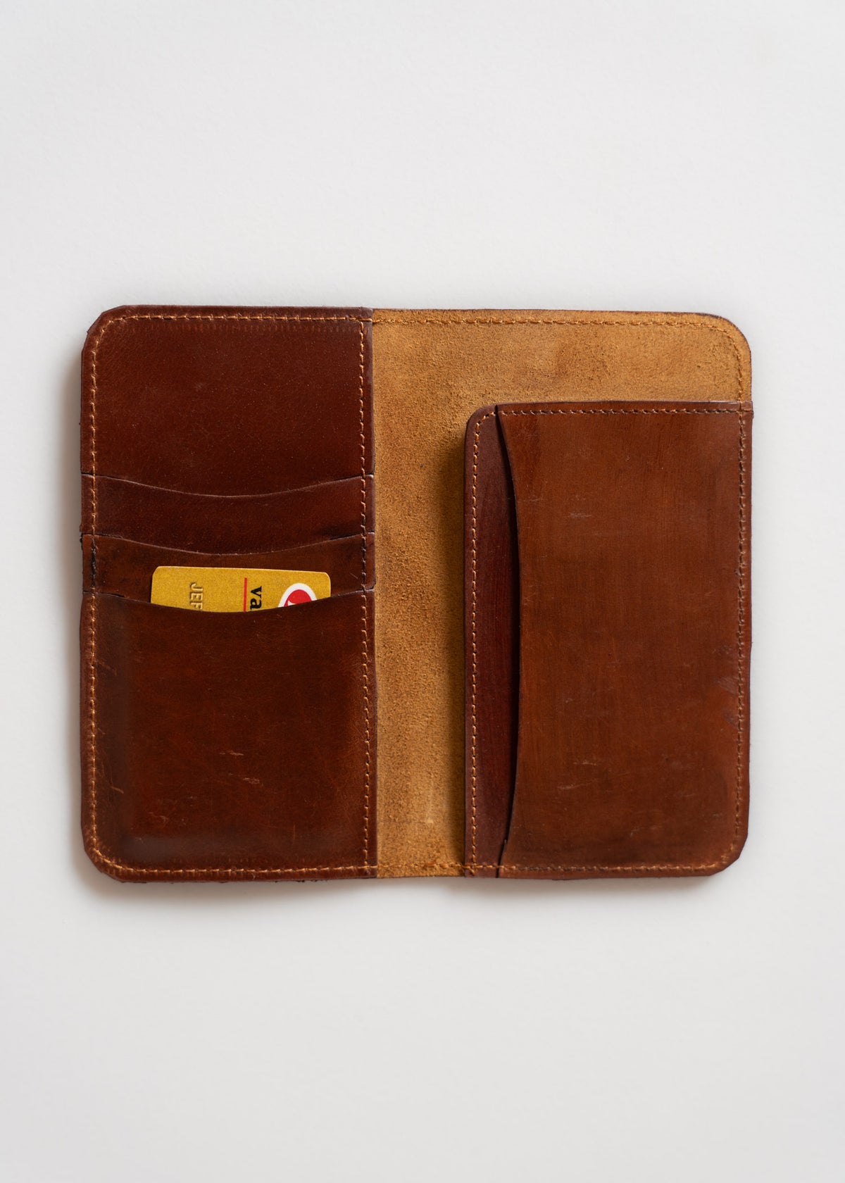 Open brown leather wallet with card slots, holding a yellow card, on a white background. Simple and elegant design.