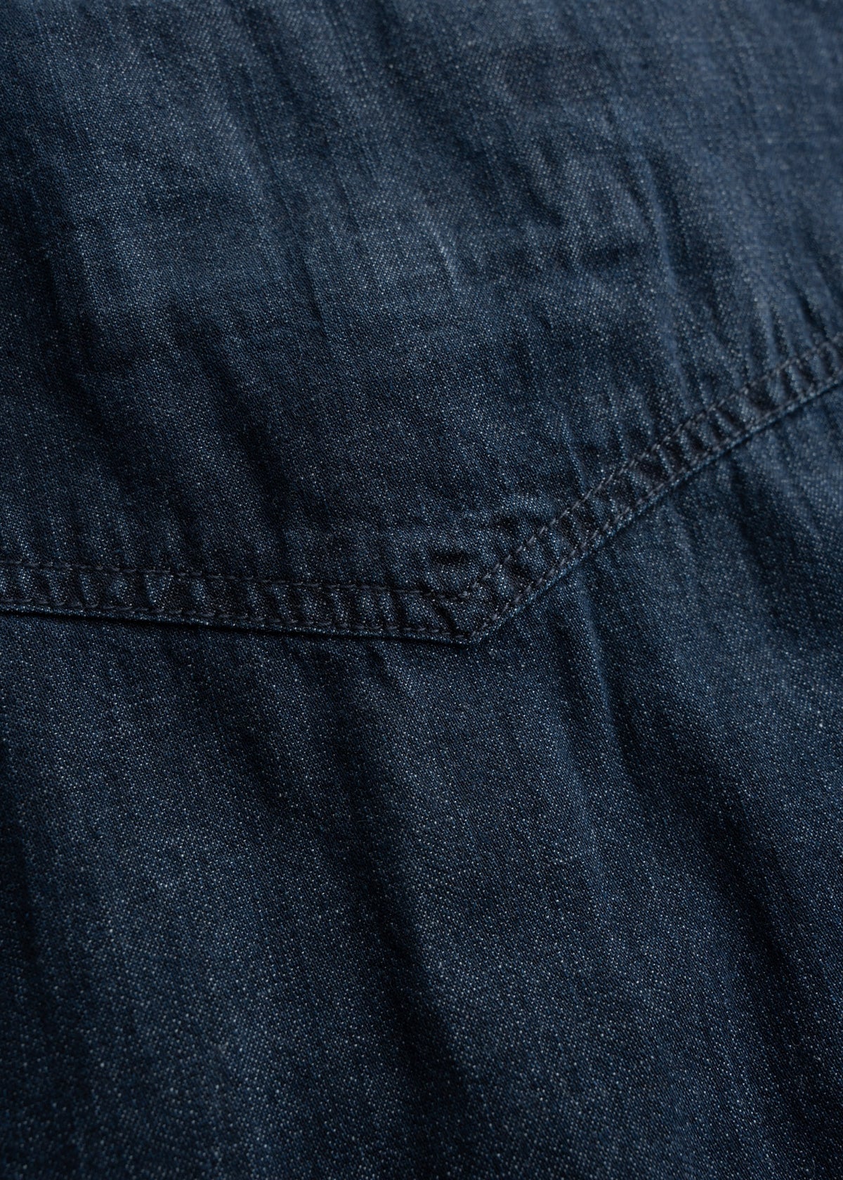 Close-up of dark blue denim fabric with visible stitching and texture, highlighting the material's rugged and classic appearance.