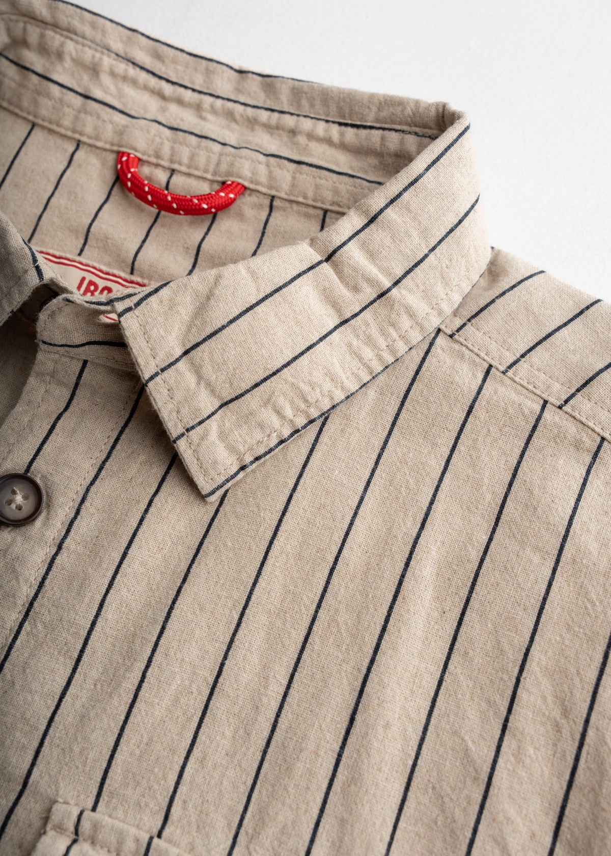 Close-up of a beige pinstripe shirt with a red loop inside the collar, showcasing button details and fabric texture.