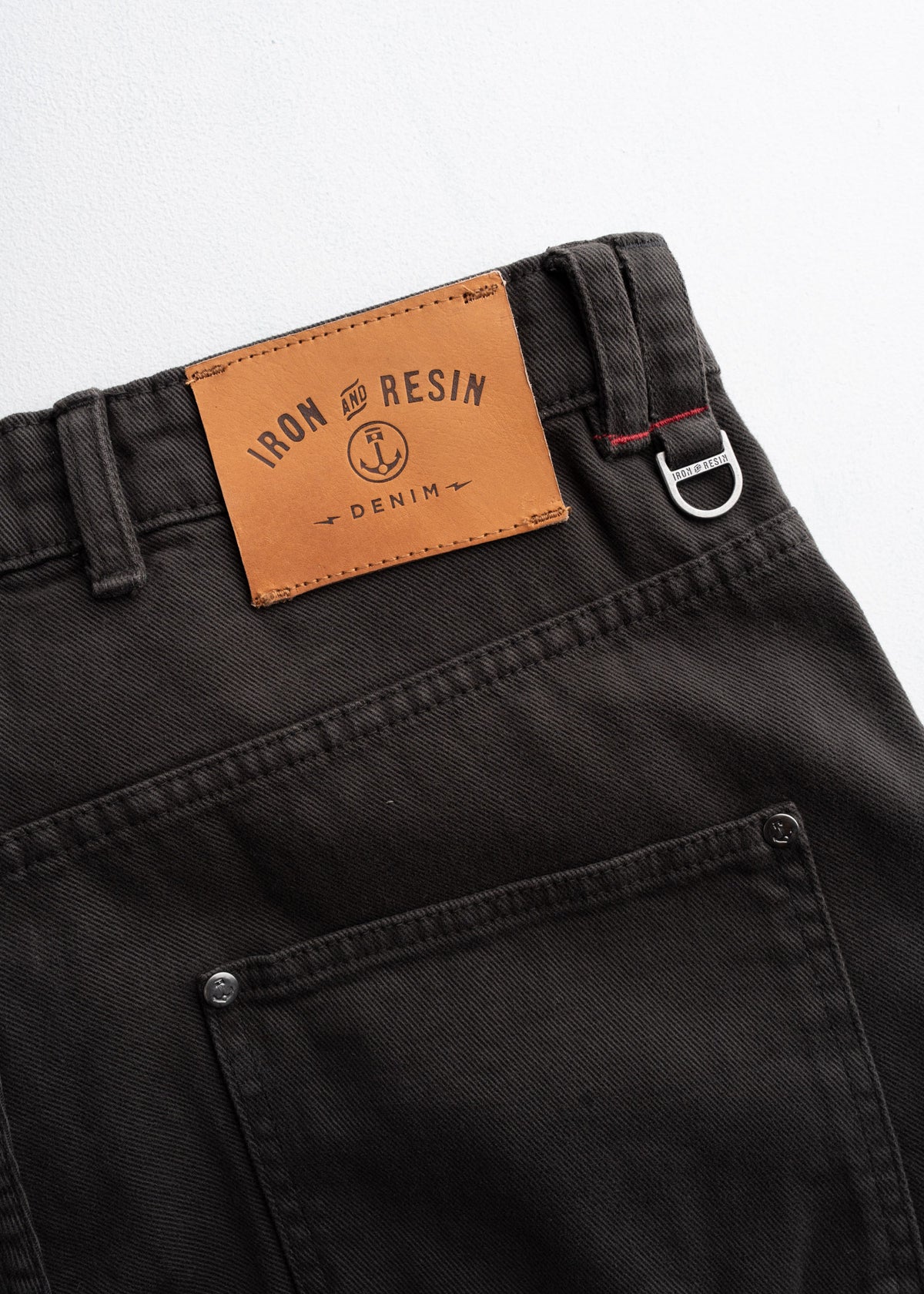 Close-up of black denim jeans with a brown "Iron and Resin" label and metal ring detail on the belt loop.