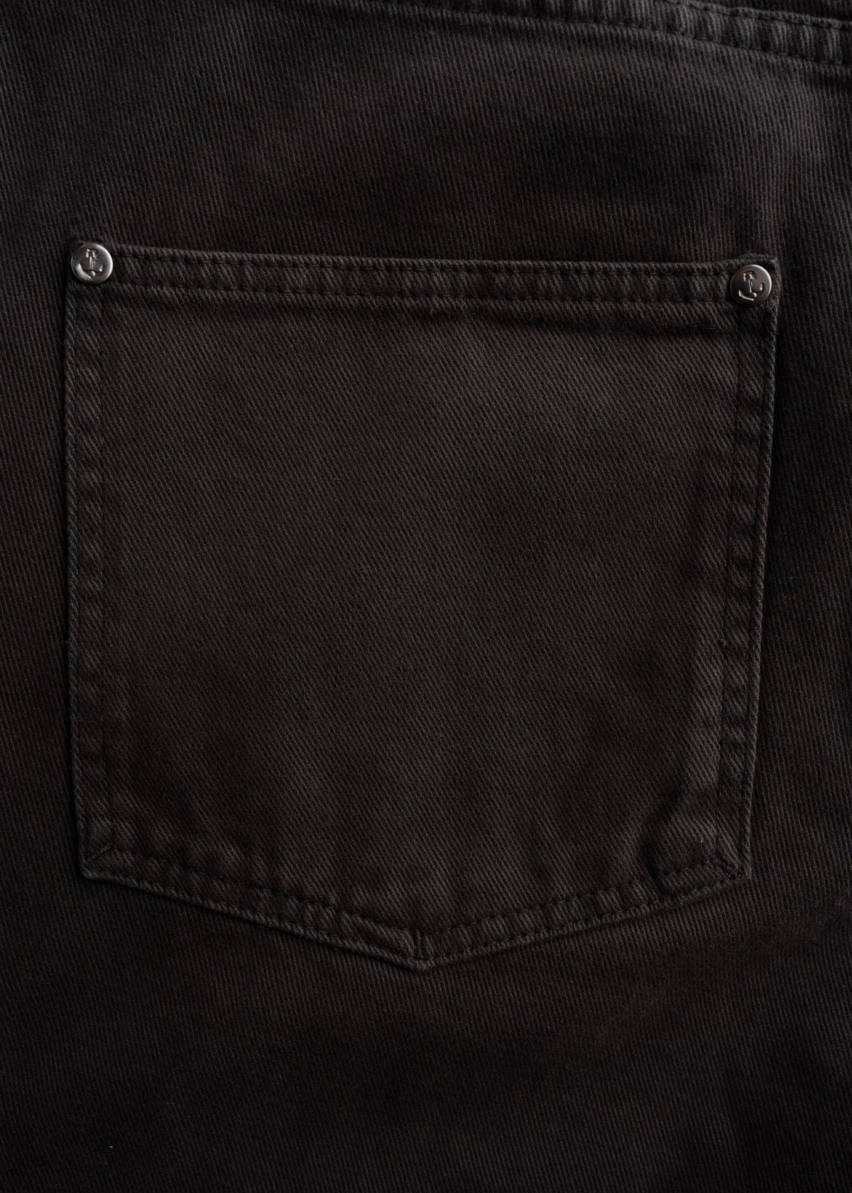 Close-up of a black denim pocket with visible stitching and metal rivets, showcasing texture and craftsmanship.