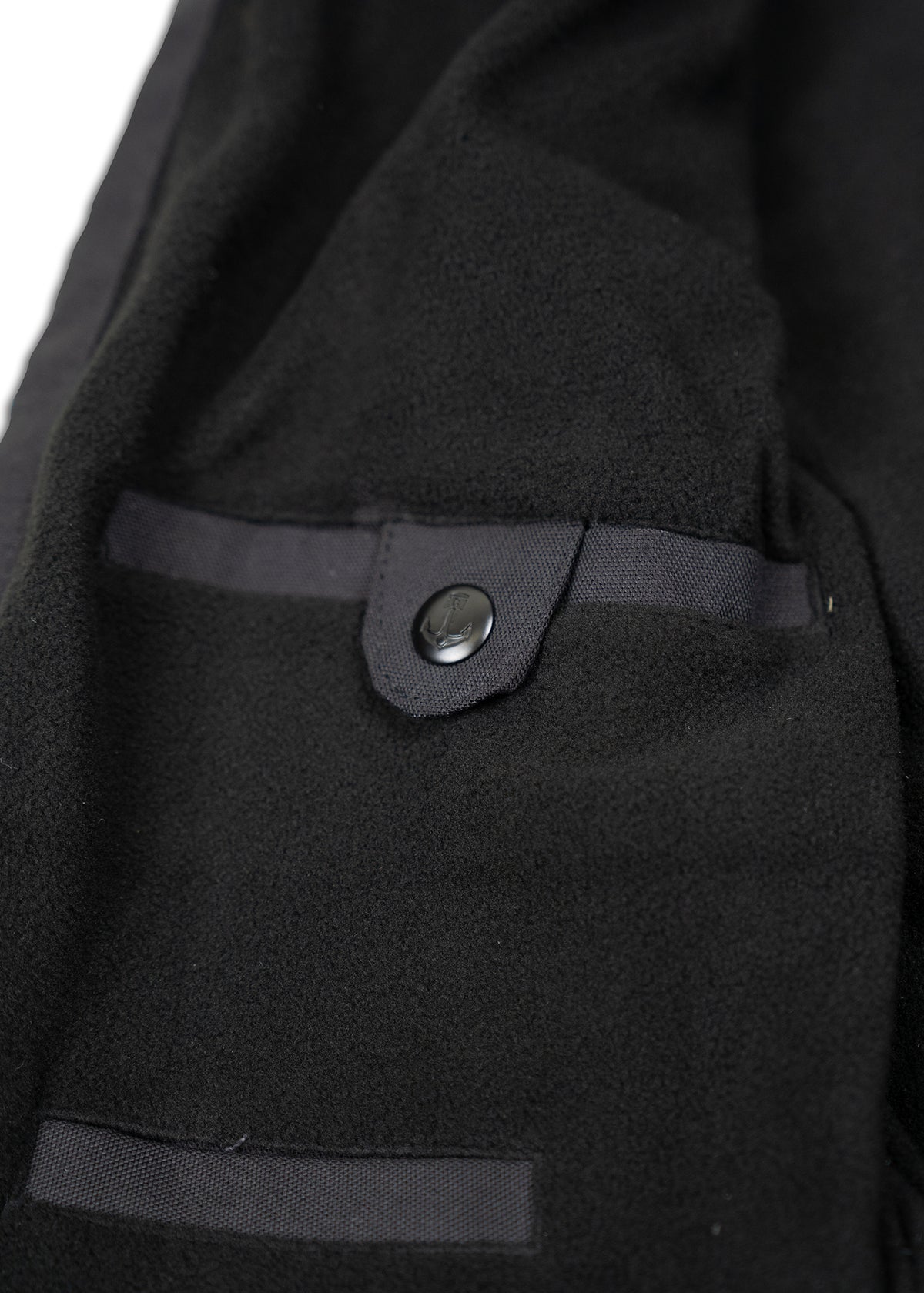 Close-up of a black fleece jacket's interior pocket with a button closure, highlighting its texture and craftsmanship.