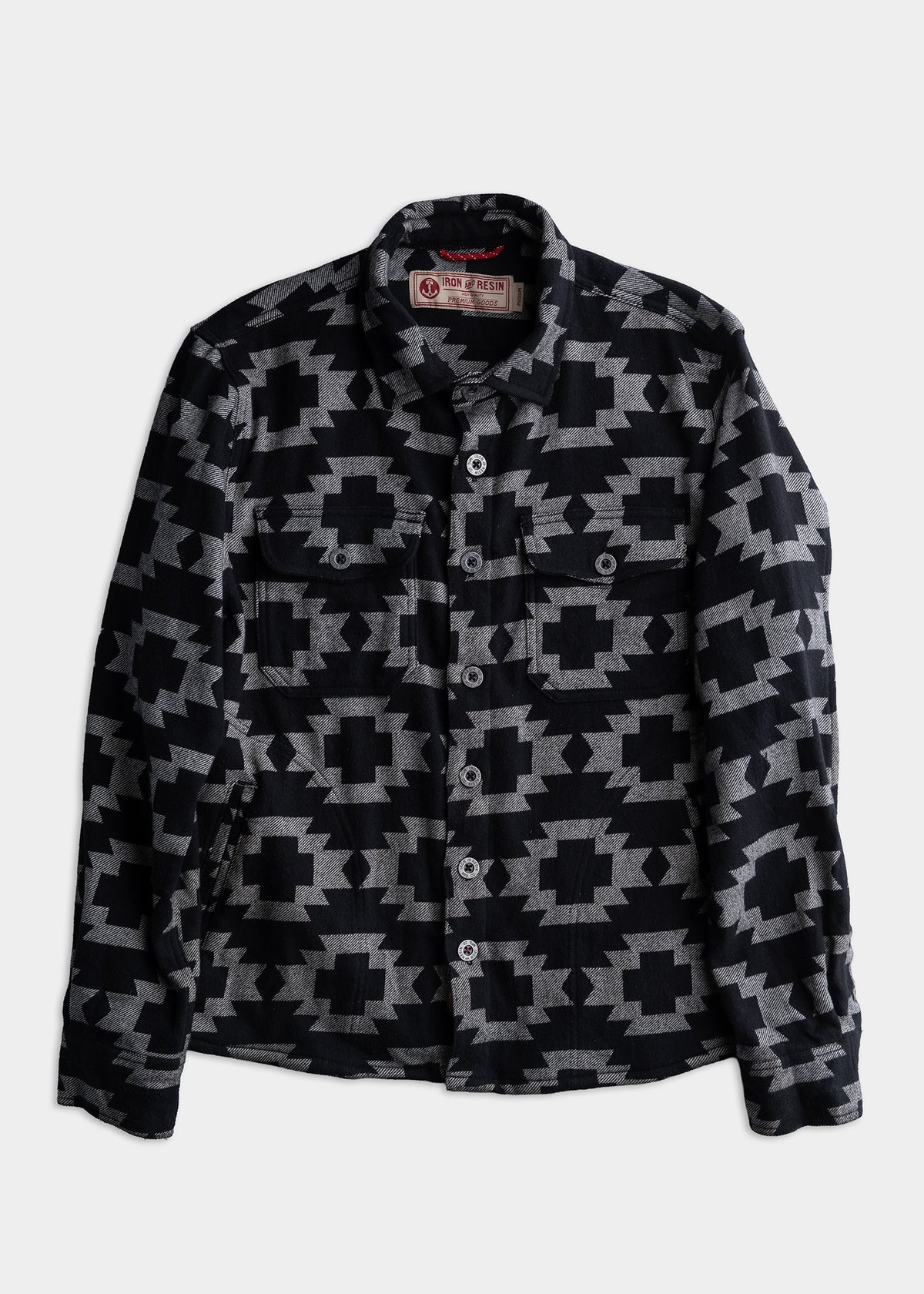 Black and grey geometric patterned shirt with buttons, featuring two chest pockets, displayed on a plain white background.