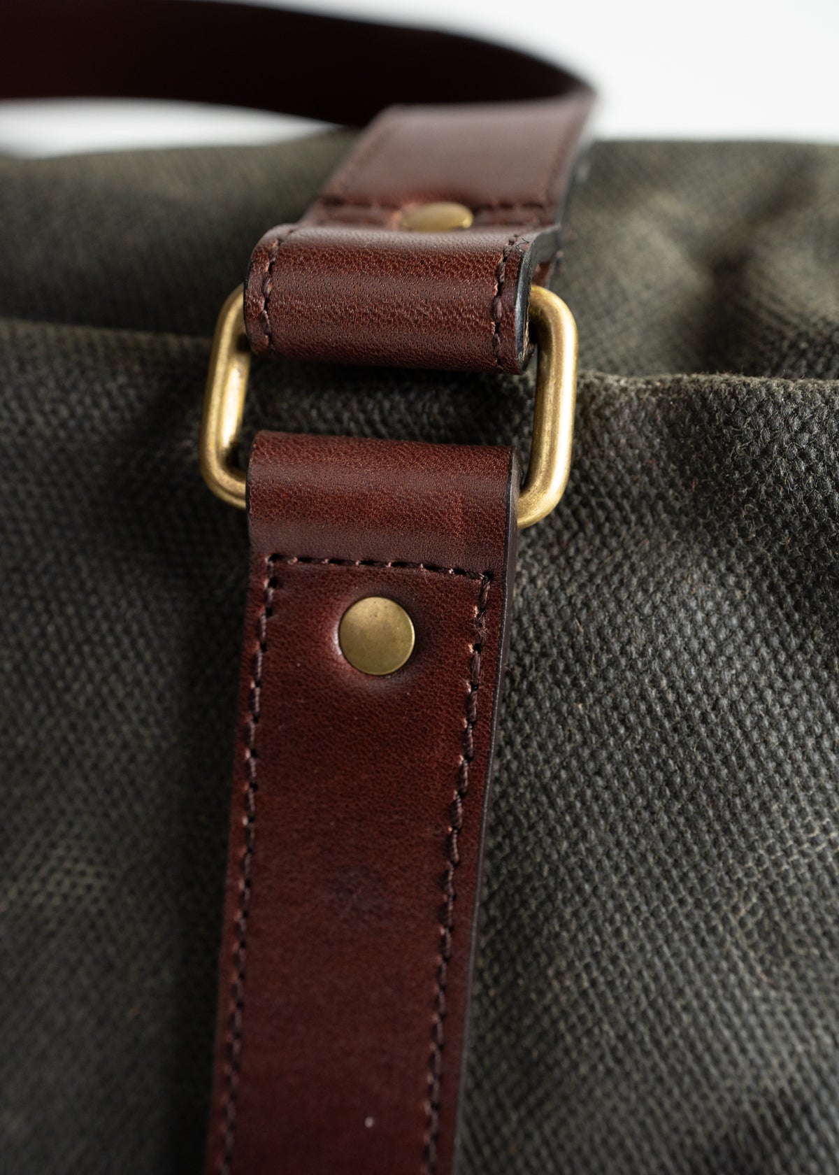 Close-up of a brown leather strap with brass buckle on a textured green canvas bag, highlighting craftsmanship and material.