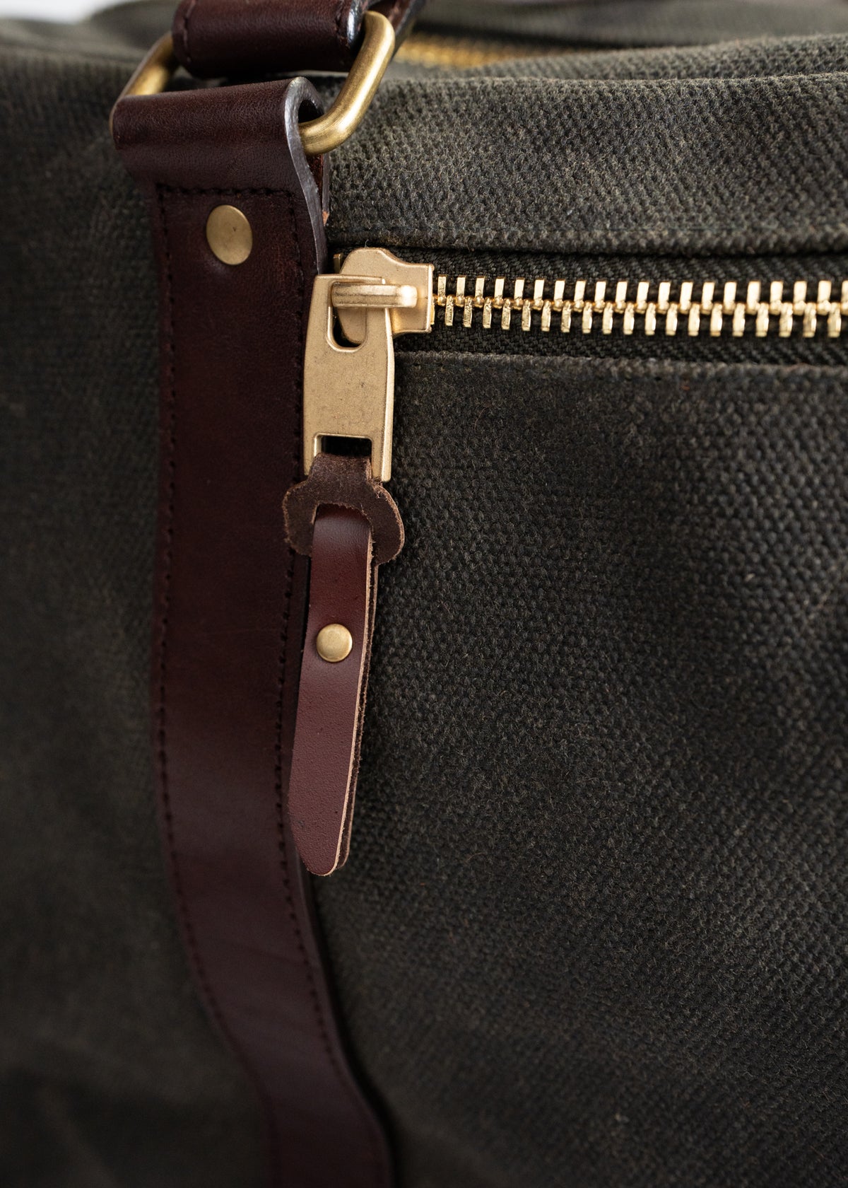 Close-up of a canvas bag with a leather strap and brass zipper, highlighting the durable materials and craftsmanship.