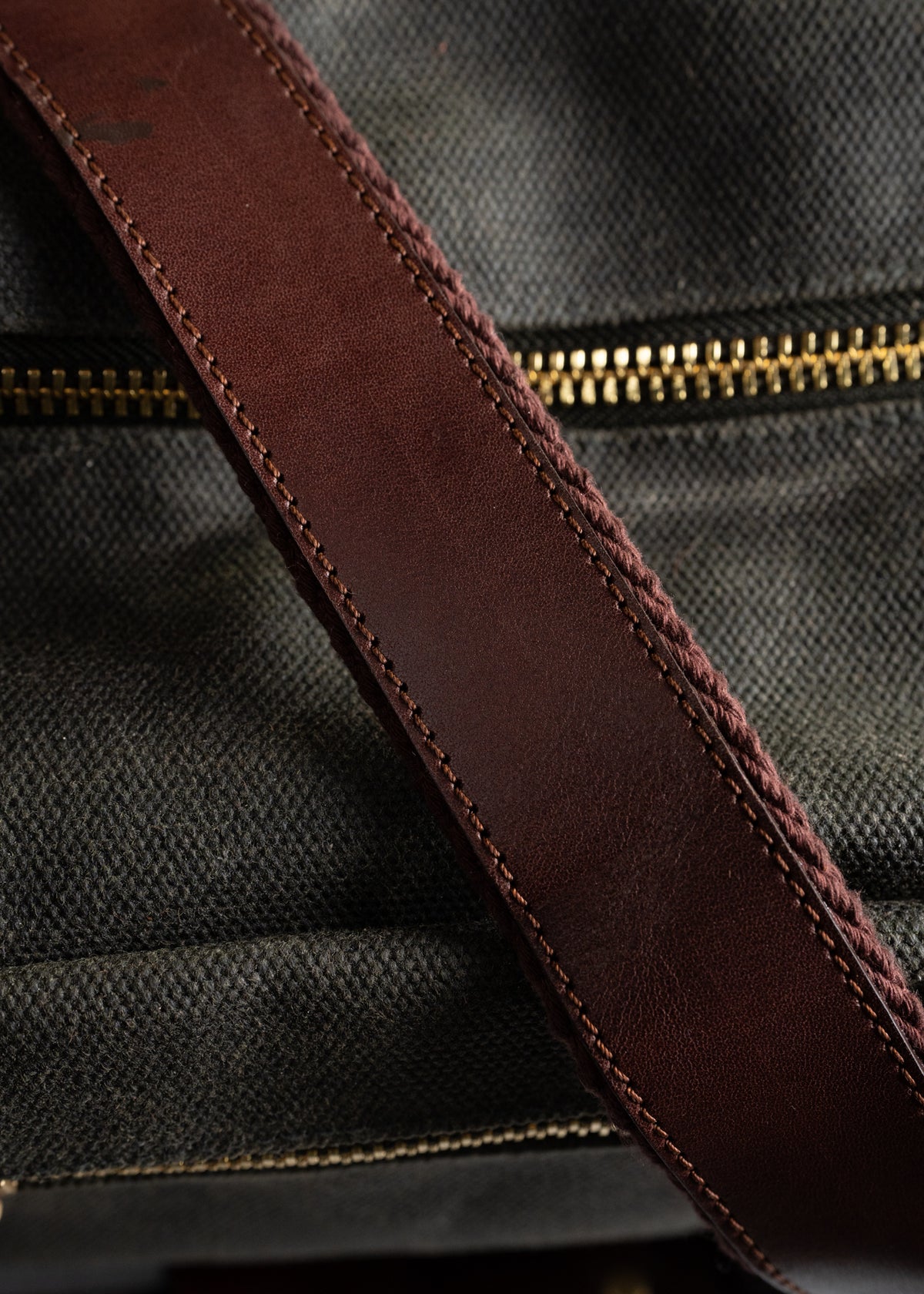 Close-up of a brown leather strap on a textured fabric bag with a visible gold zipper, highlighting craftsmanship and detail.