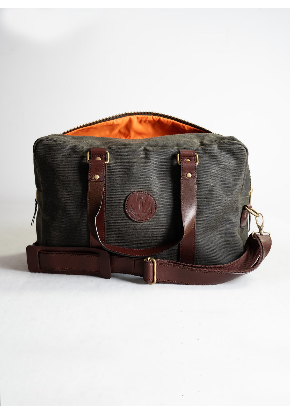 A stylish canvas duffel bag with brown leather straps and an orange interior, perfect for travel or weekend getaways.