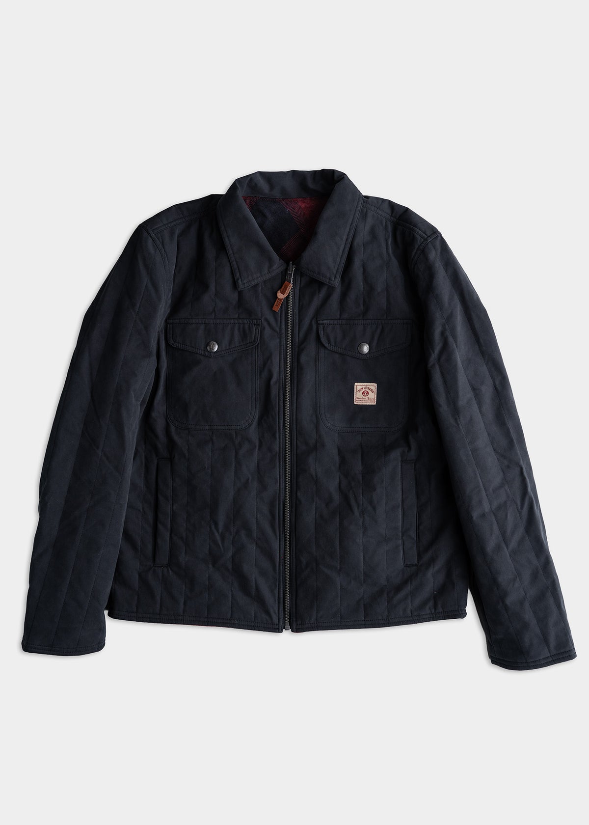 Dark quilted jacket with a zipper, two chest pockets, and a small logo patch on the front. Simple and stylish outerwear.