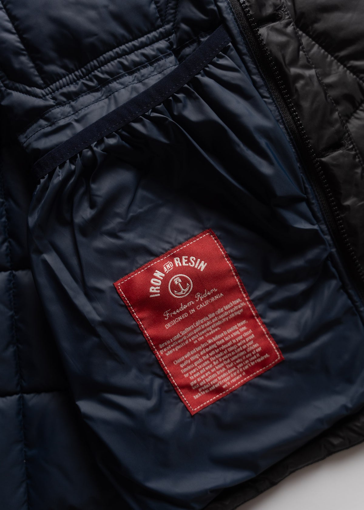 Close-up of a black jacket's interior, showing a red Iron and Resin label with text, highlighting its design in California.