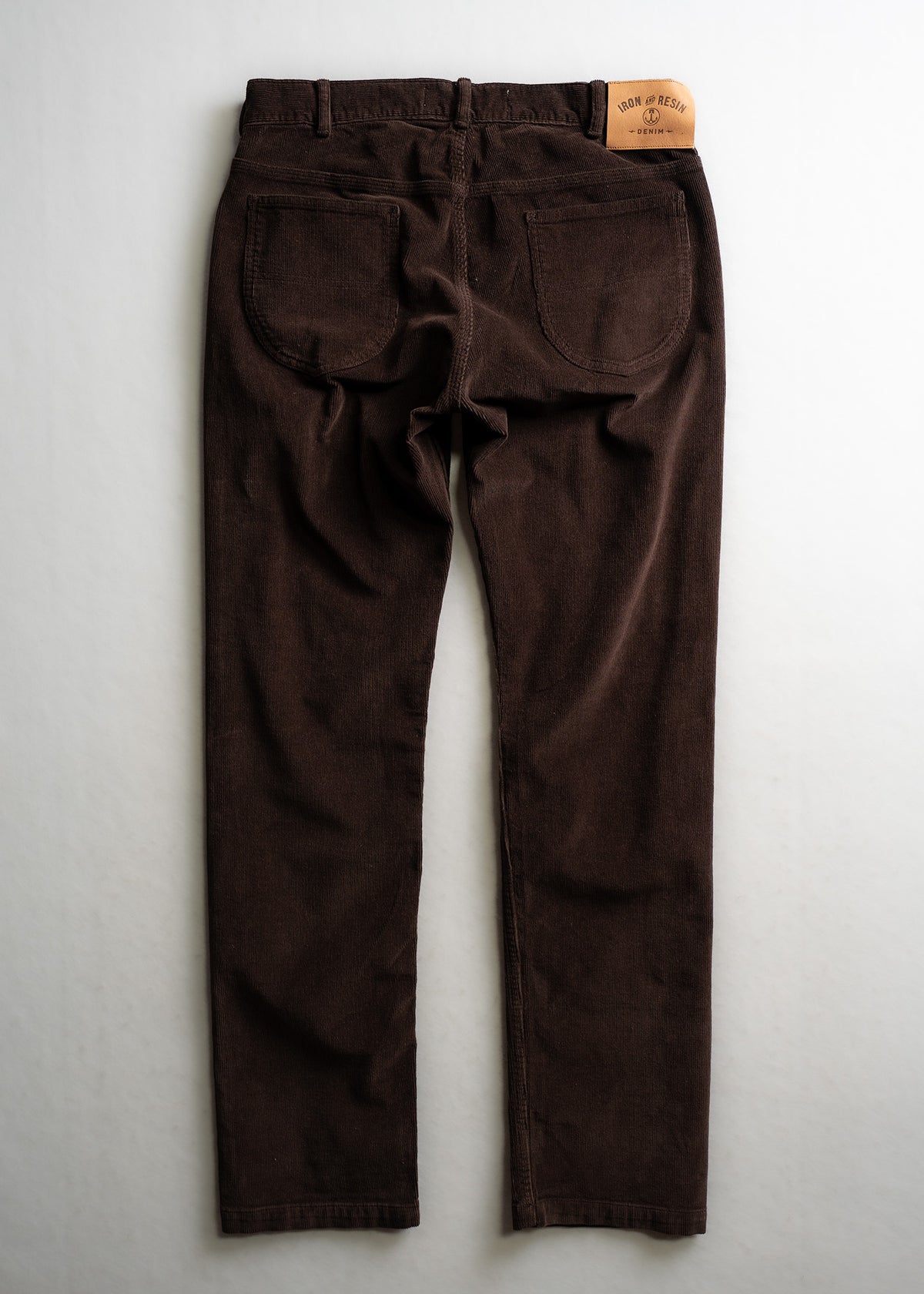 Brown corduroy pants with two back pockets, displayed flat on a light background. A leather patch reads "Iron & Resin Denim."