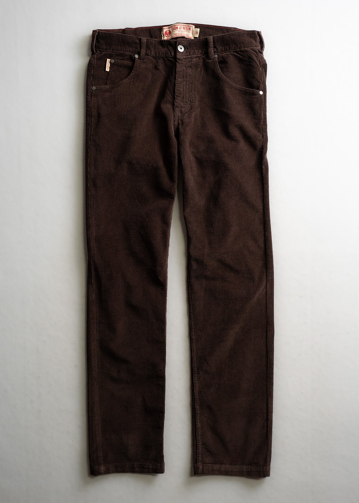 Brown corduroy pants with a button closure, front pockets, and a branded label on the waistband, laid flat on a light surface.