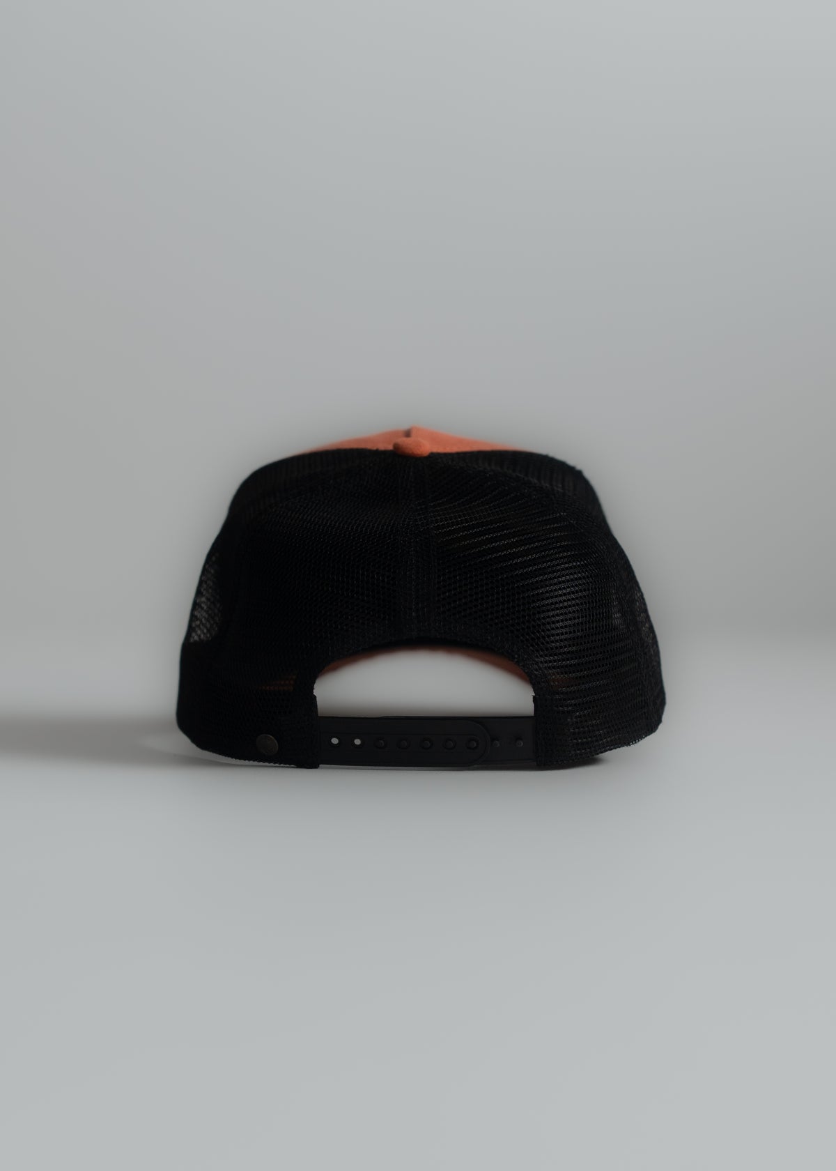A black mesh trucker hat with an adjustable strap is shown from the back on a plain gray background.