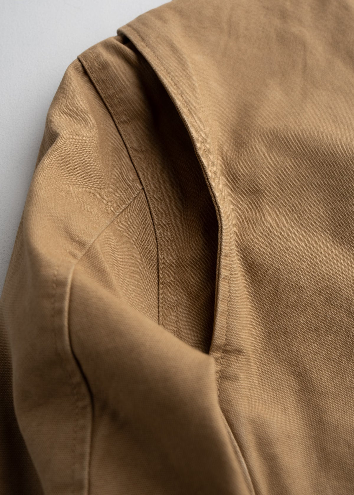 Close-up of a brown jacket's shoulder and sleeve, highlighting the stitching and fabric texture against a light background.