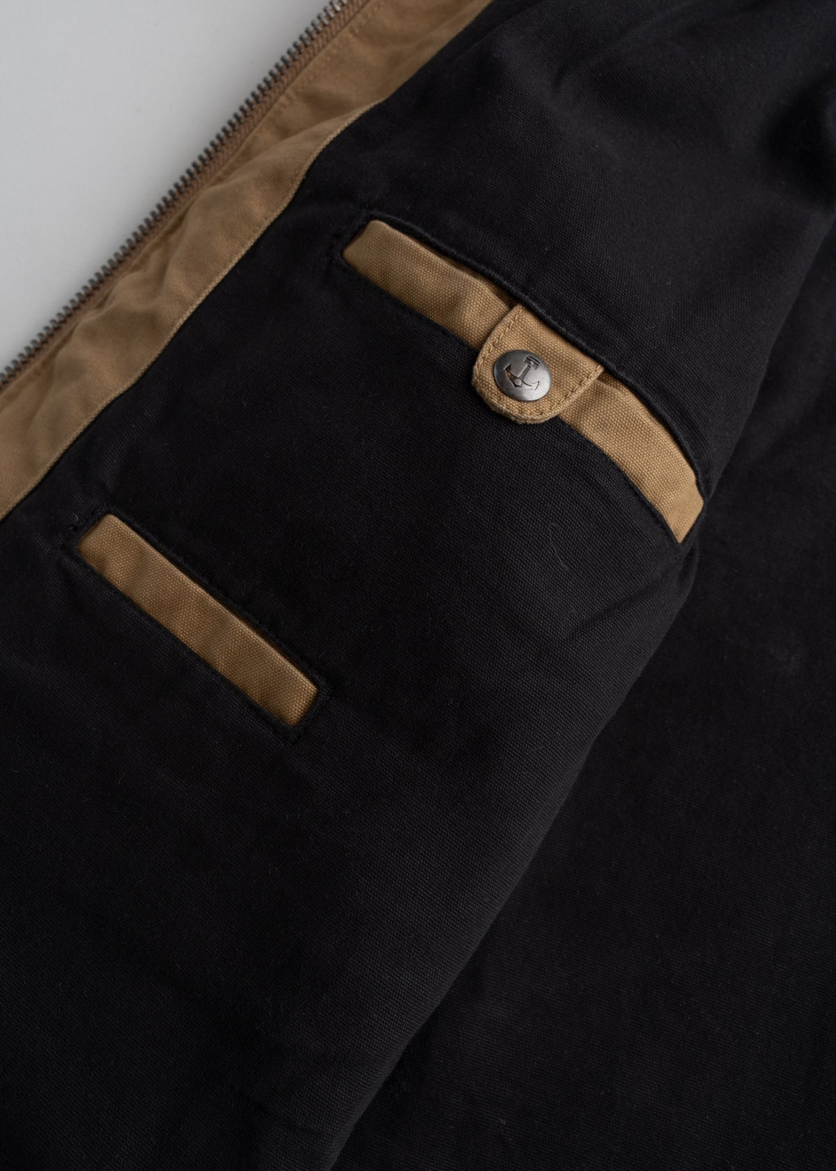 Black jacket with brown accents, featuring a buttoned pocket and zipper detail, showcasing a stylish and functional design.