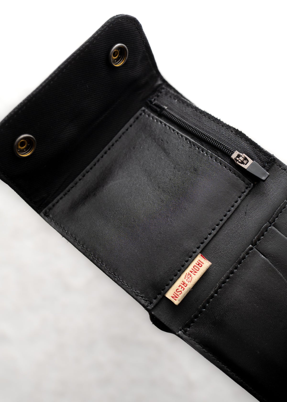Open black leather wallet with snap buttons, zippered pocket, and "Iron Resin" label visible inside against a light background.