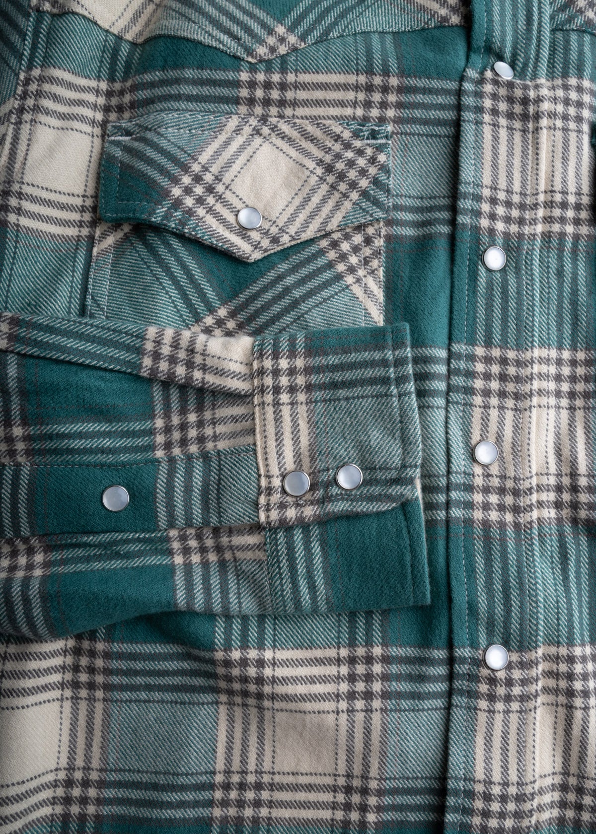 Close-up of a green and beige plaid flannel shirt with snap buttons and a chest pocket, showcasing its detailed pattern.