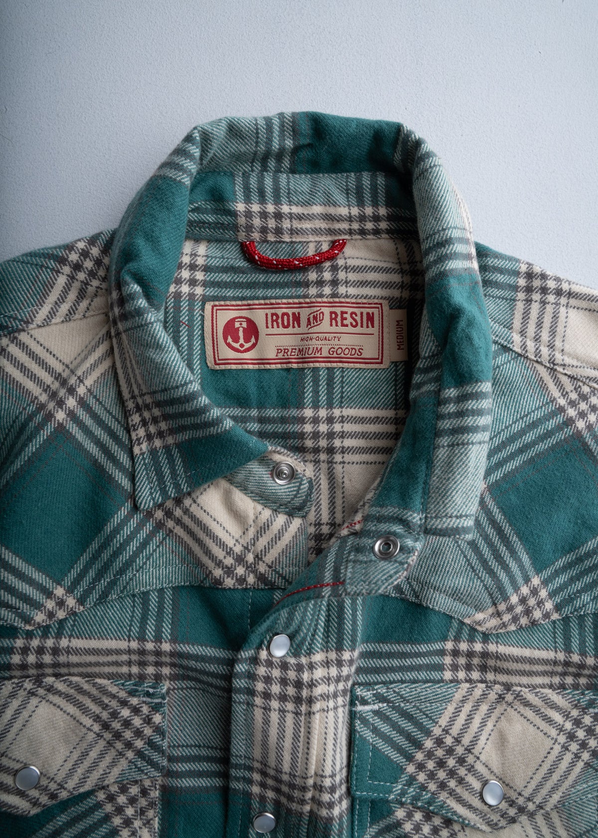 Green plaid shirt with snap buttons and "Iron and Resin" label, showcasing premium quality and classic style against a plain backdrop.
