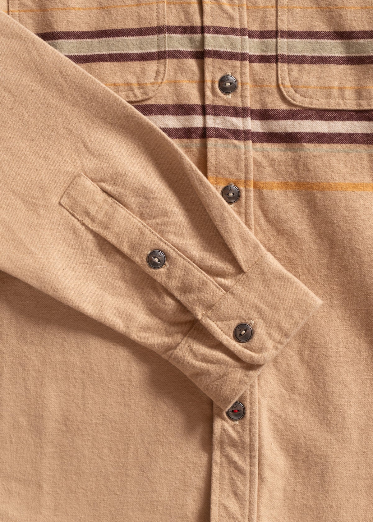 Close-up of a tan button-up shirt with maroon and yellow stripes, highlighting the sleeve and metal buttons for detail.