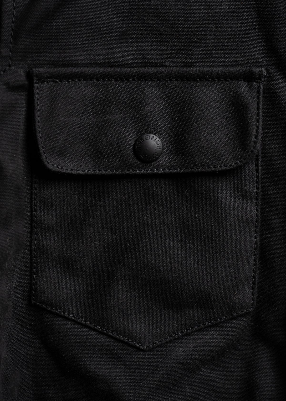 Close-up of a black fabric pocket with a buttoned flap, showcasing texture and stitching details.
