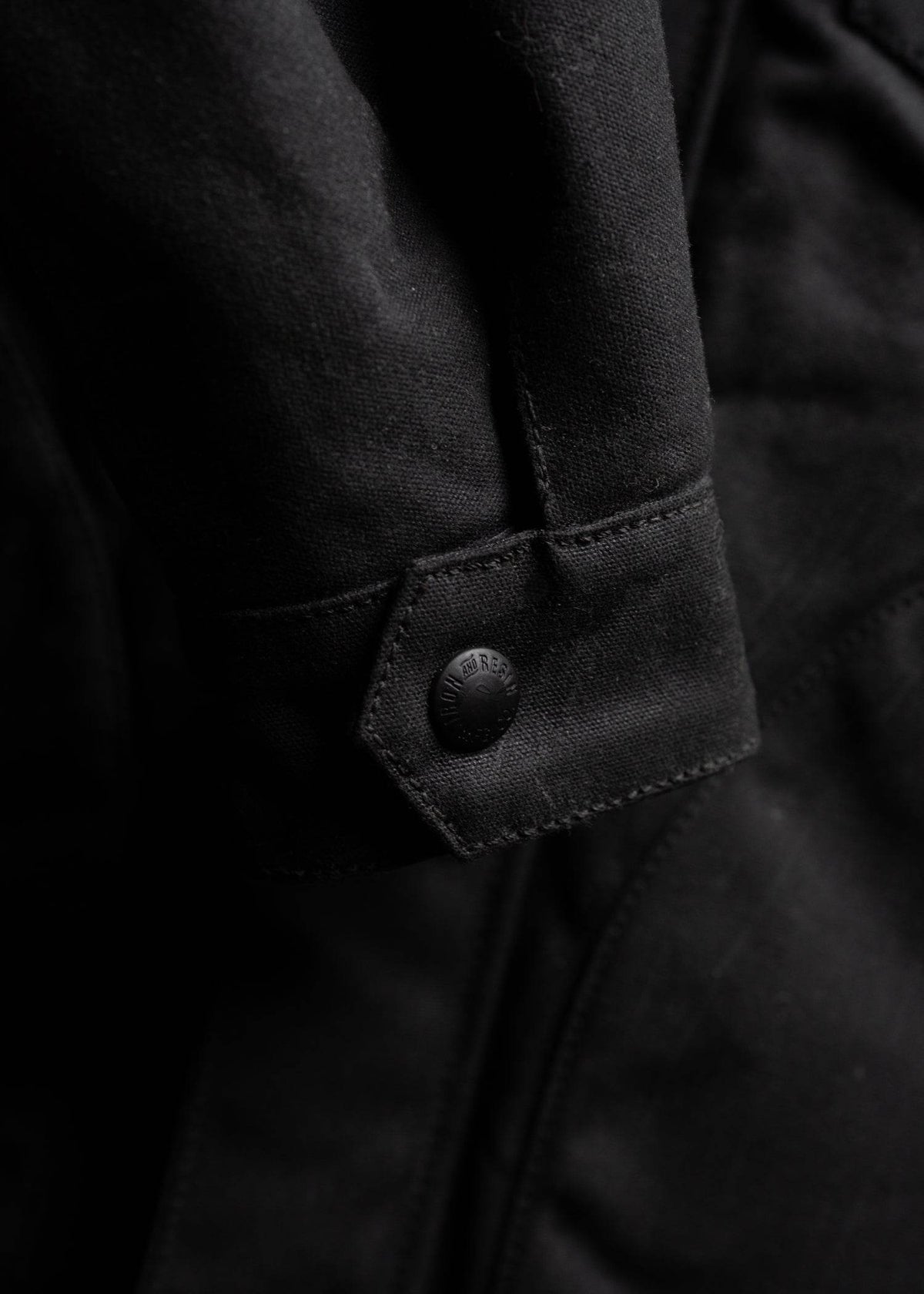 Close-up of a black jacket sleeve with a button detail, showcasing textured fabric and stitching for a sleek, modern look.