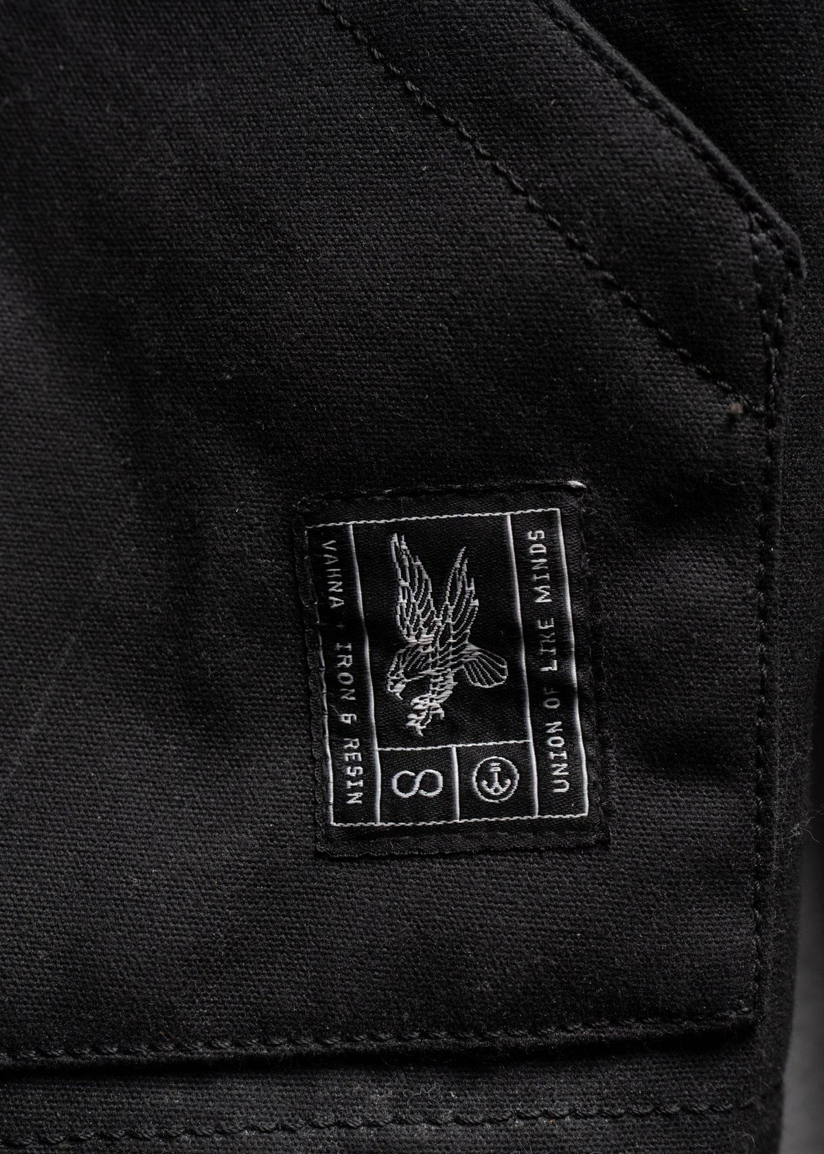 Close-up of a black fabric with a label featuring an eagle, anchor, and text "Iron & Resin" and "Union of Like Minds" in white.