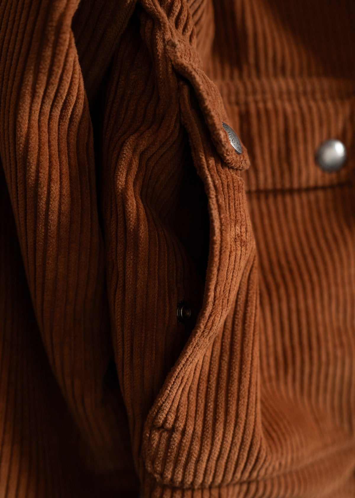 Close-up of a brown corduroy jacket with visible metal buttons, highlighting its textured fabric and rich color.