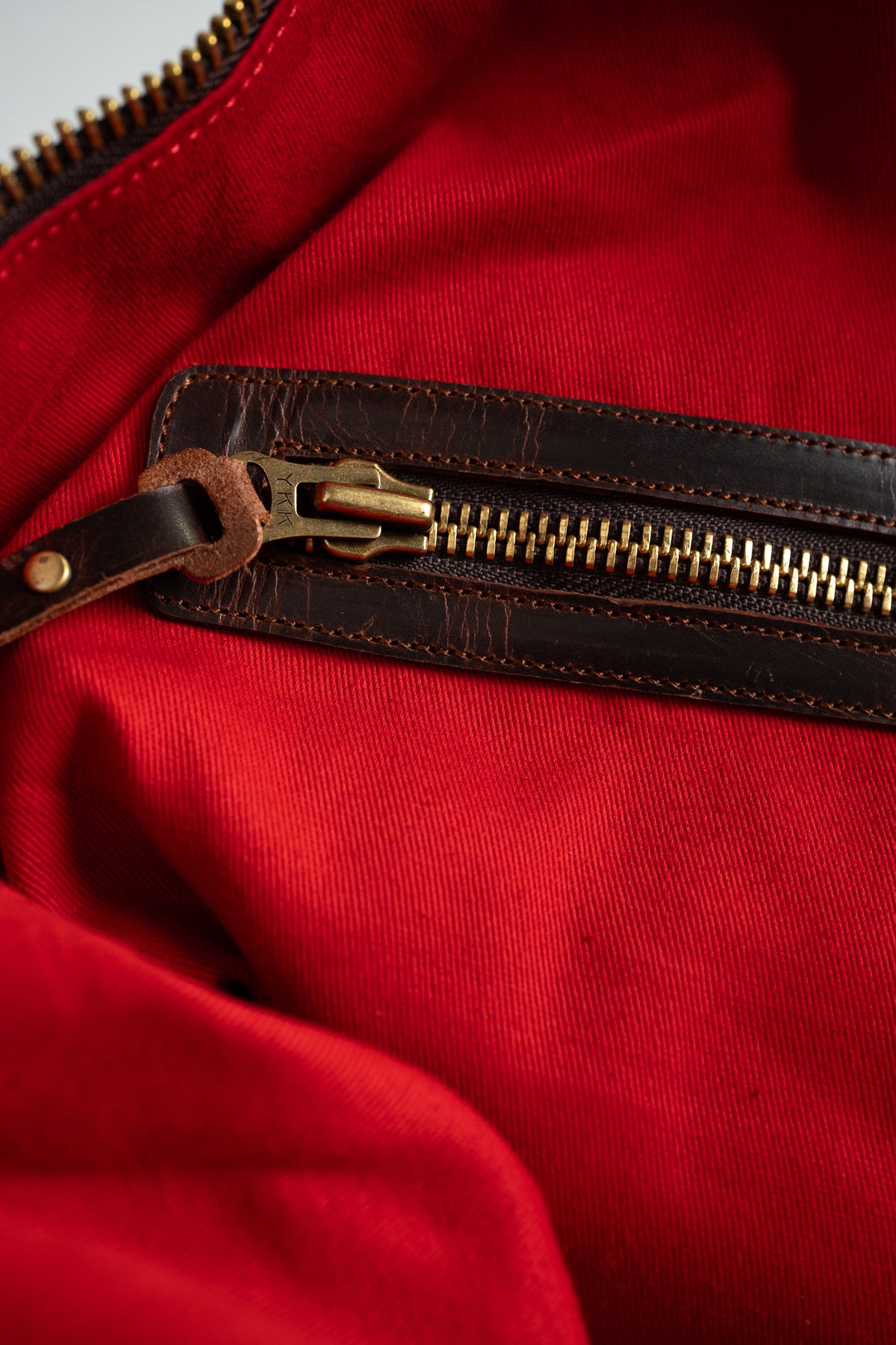 Close-up of a red fabric with a brown leather zipper, highlighting the texture and stitching details.