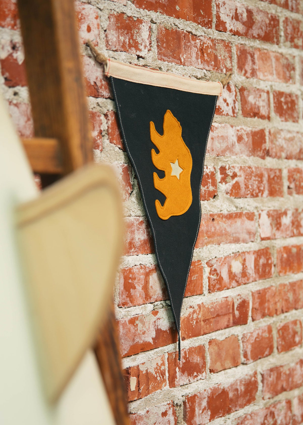 A black pennant with an orange flame and star hangs on a rustic brick wall, adding a vintage touch to the decor.