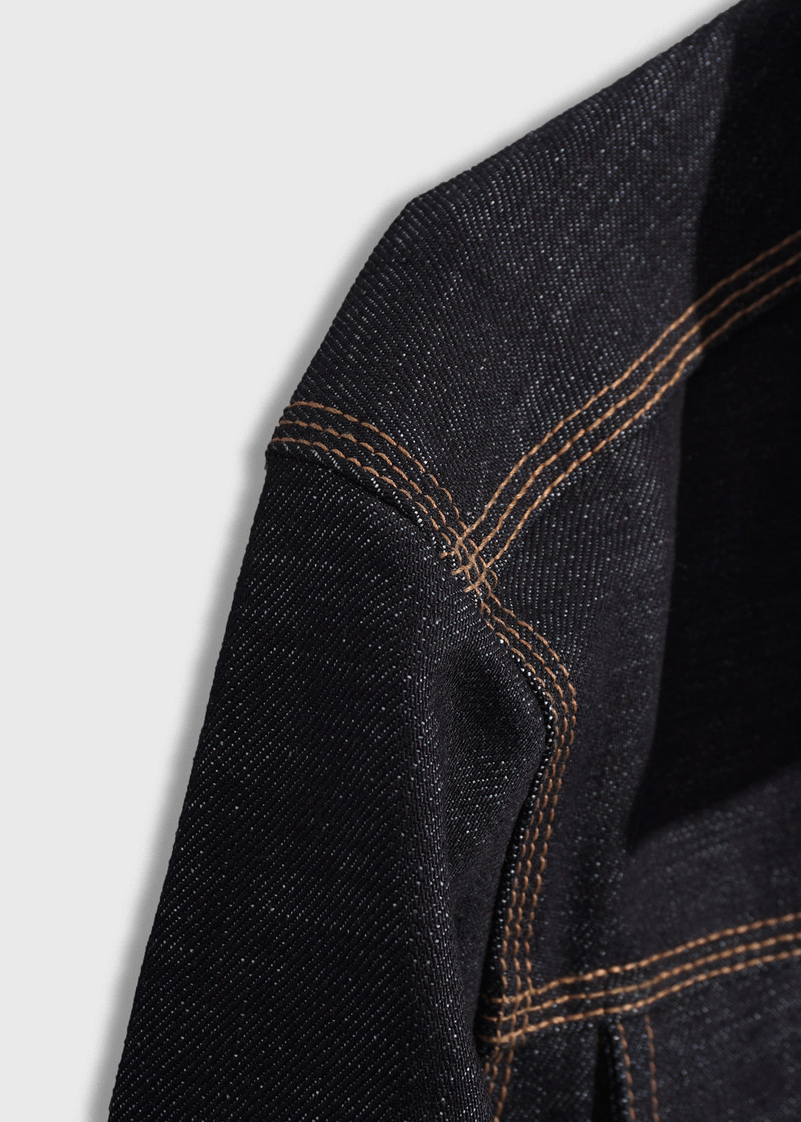 Close-up of black denim fabric with orange stitching, highlighting texture and seam details on a light gray background.
