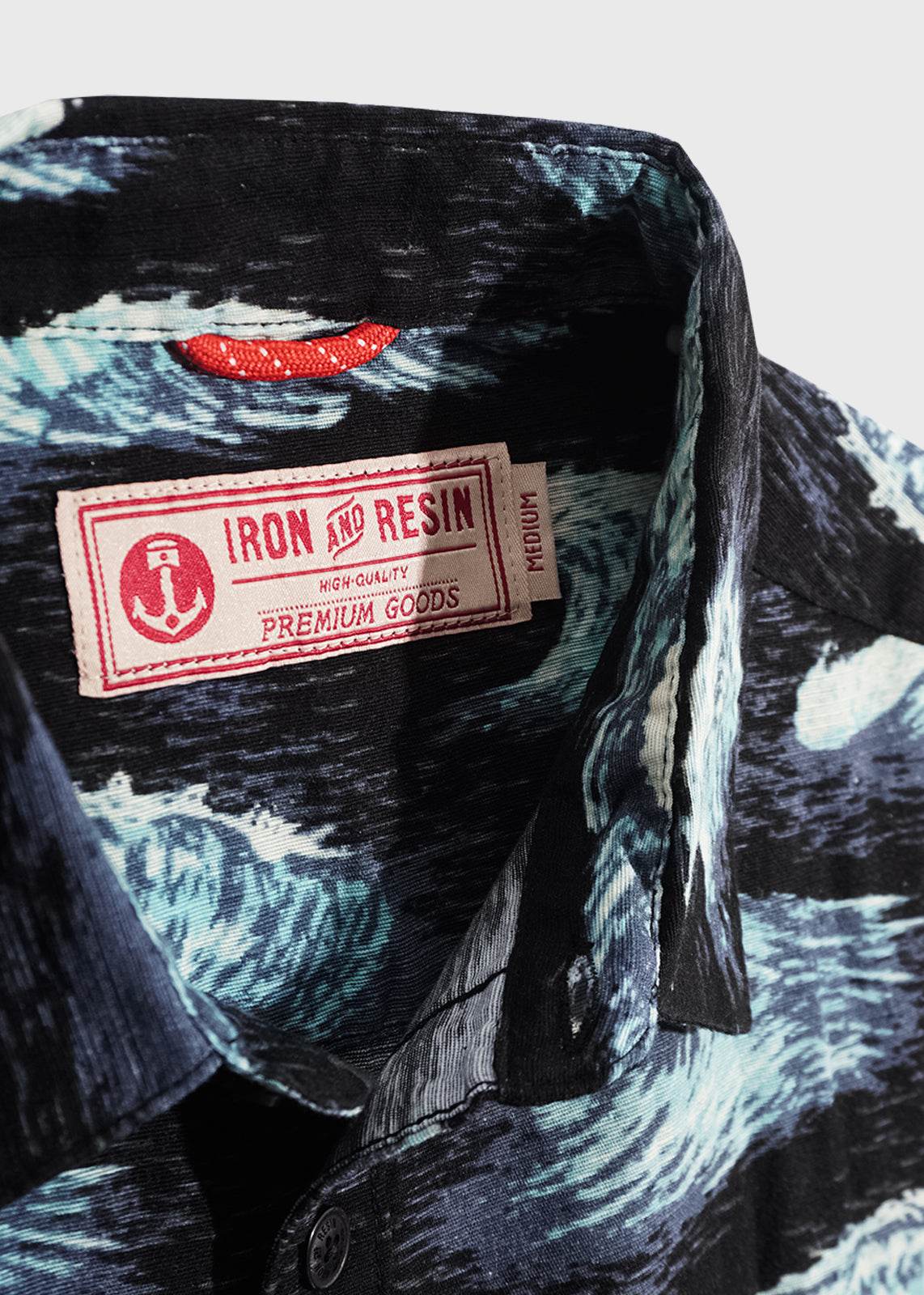Close-up of a patterned shirt collar with a red "Iron and Resin" label, featuring an anchor logo and "Premium Goods" text.