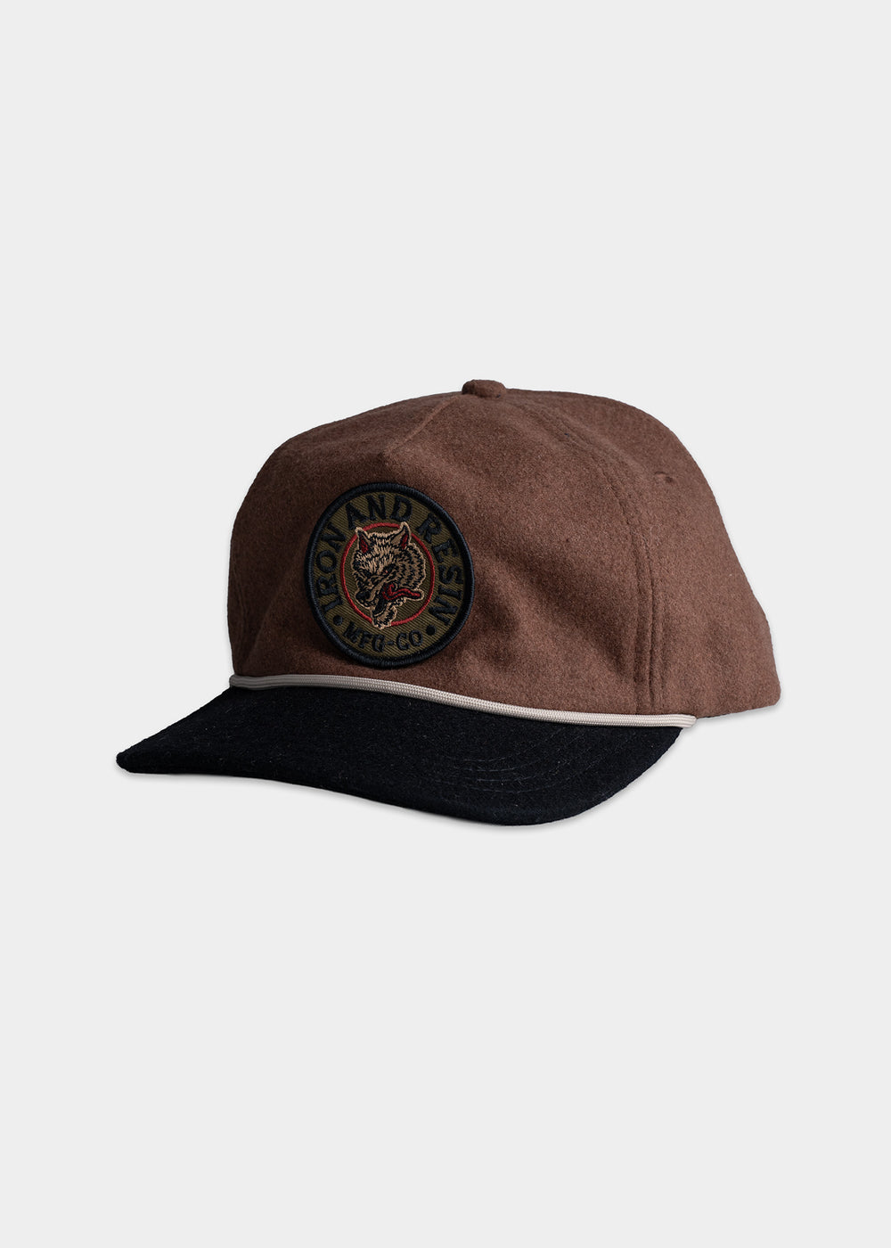Brown cap with a black brim, featuring an embroidered wolf patch labeled "Iron and Resin MFG CO" on the front.