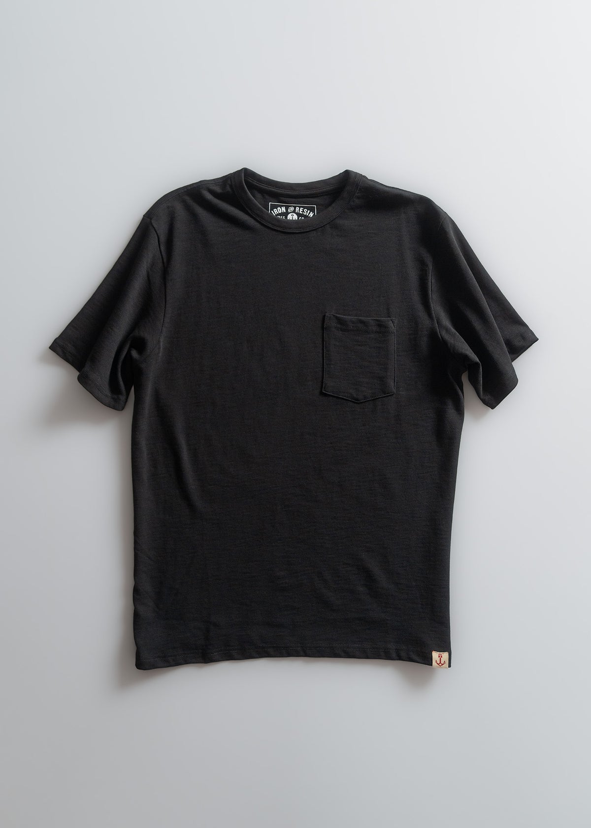 A black T-shirt with a chest pocket, displayed on a light background. The label inside reads "Iron & Resin."
