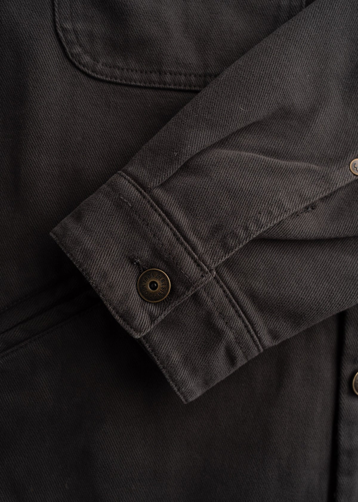 Close-up of a dark brown jacket sleeve with a button detail, showcasing textured fabric and stitching.