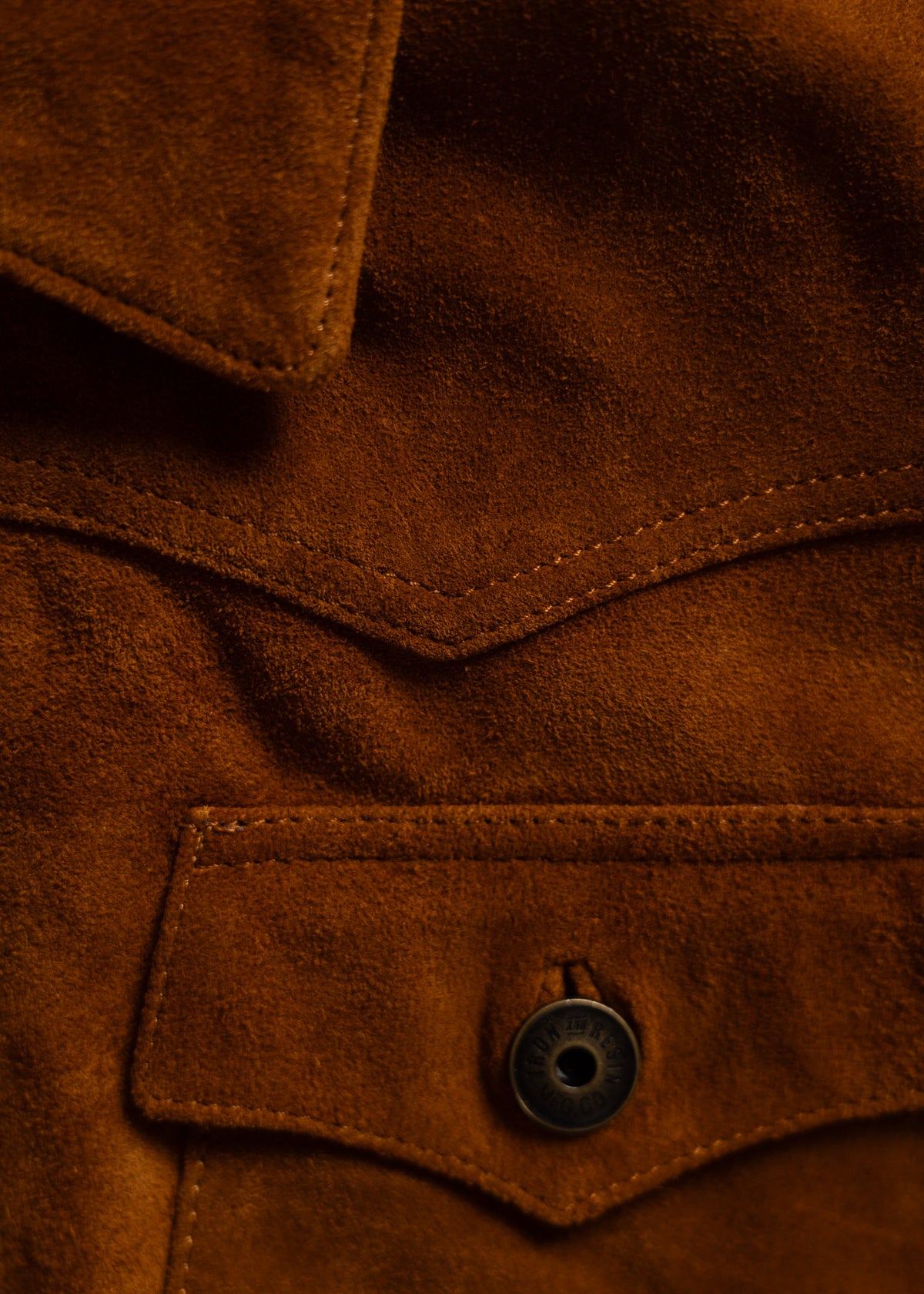 Close-up of a brown suede jacket with a visible collar, pocket flap, and button, highlighting the texture and stitching details.