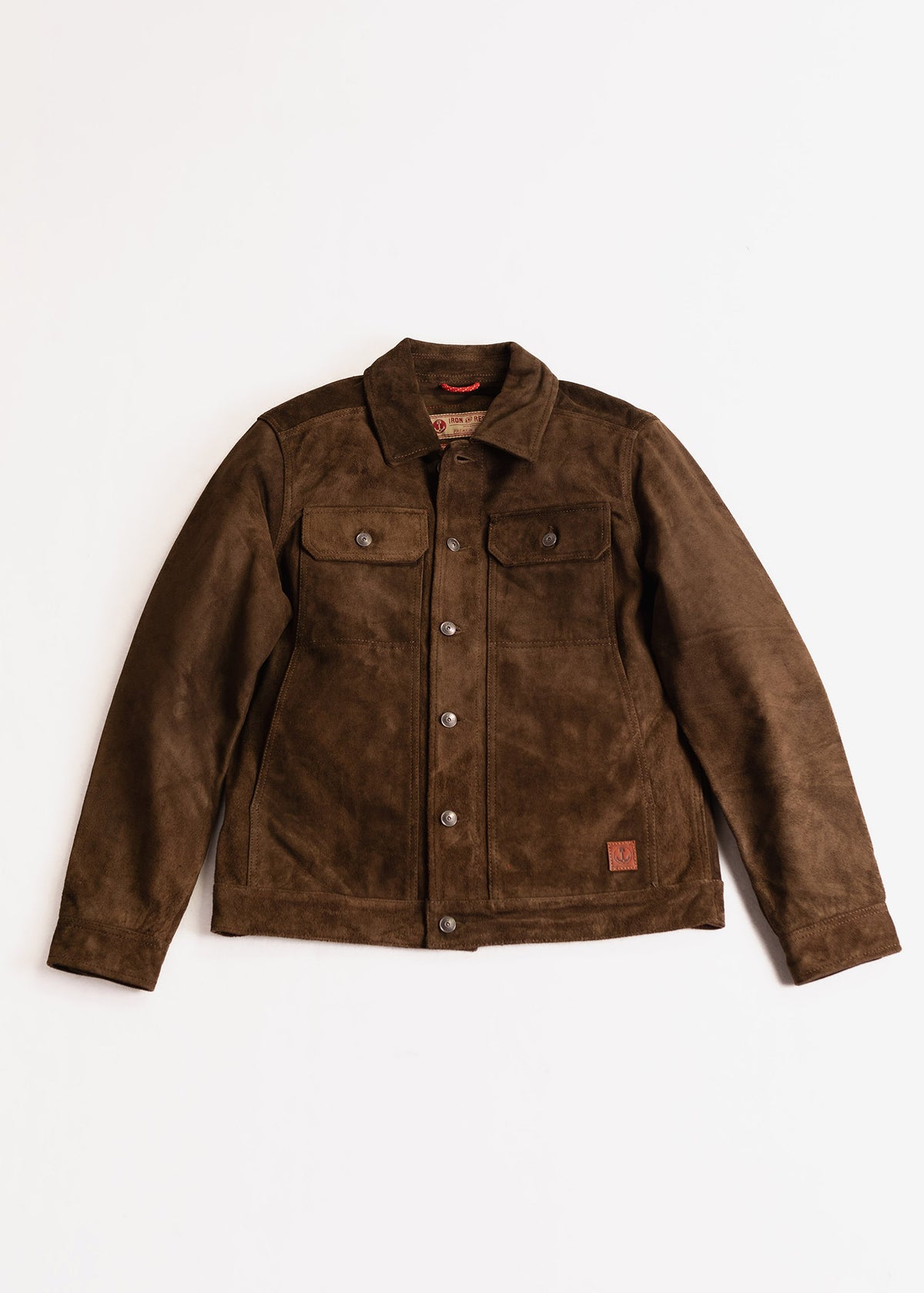 Brown suede jacket with button closure, two chest pockets, and a small leather patch on the bottom right, laid flat on white.