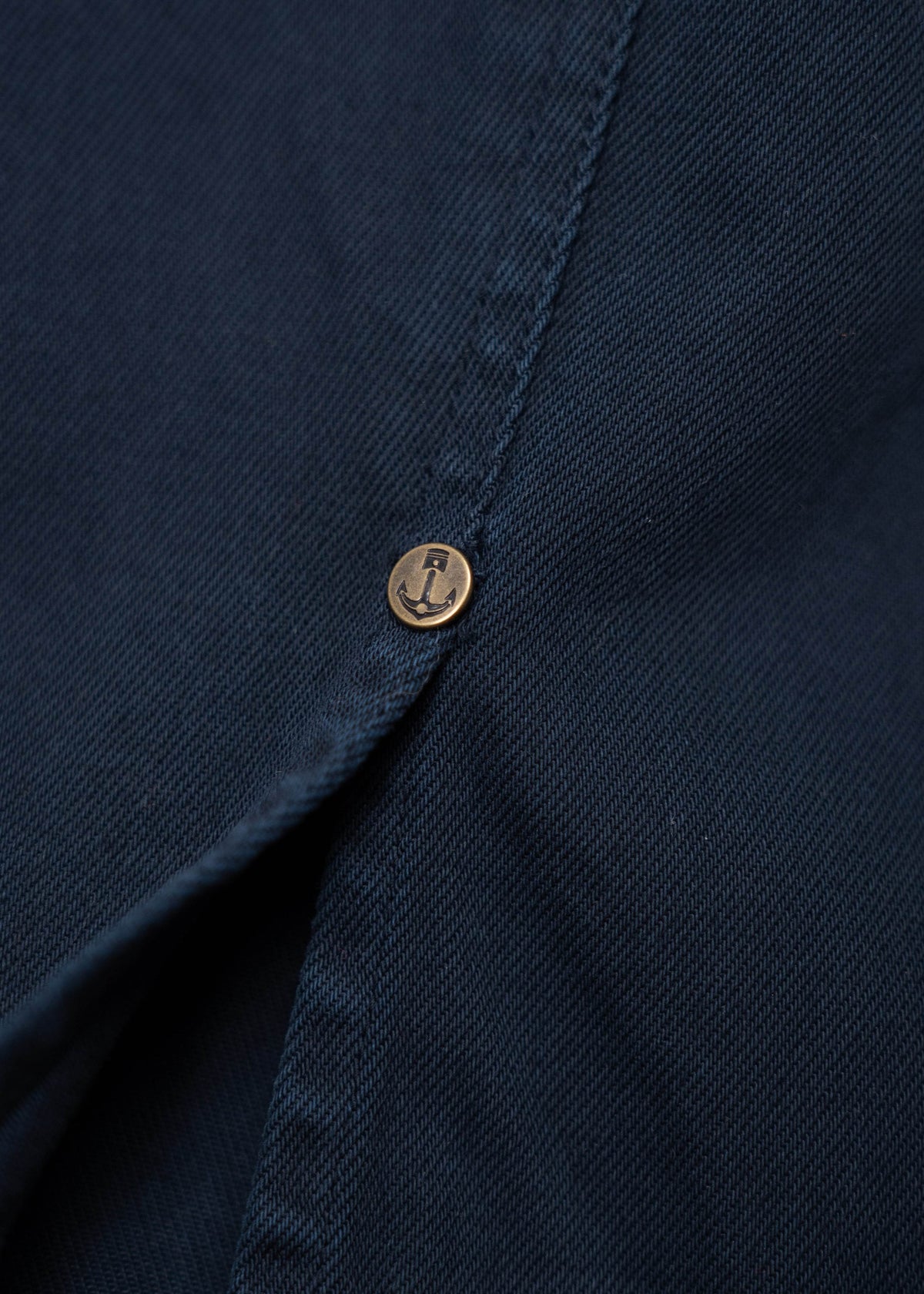 Close-up of a navy blue fabric with a small brass button featuring an anchor design, highlighting texture and nautical detail.