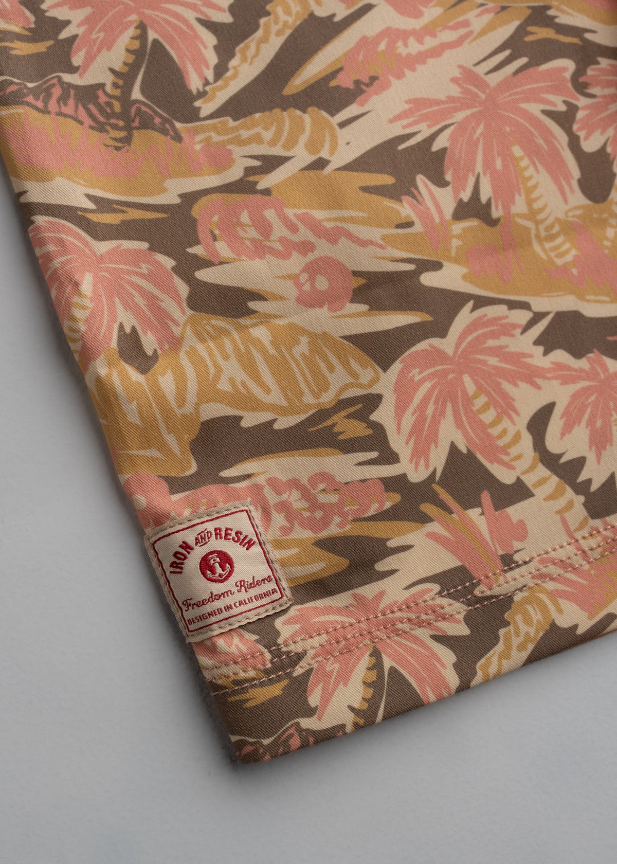 Close-up of a fabric with tropical palm patterns in pink and brown. A label reads "Iron and Resin, Freedom Riders, California."