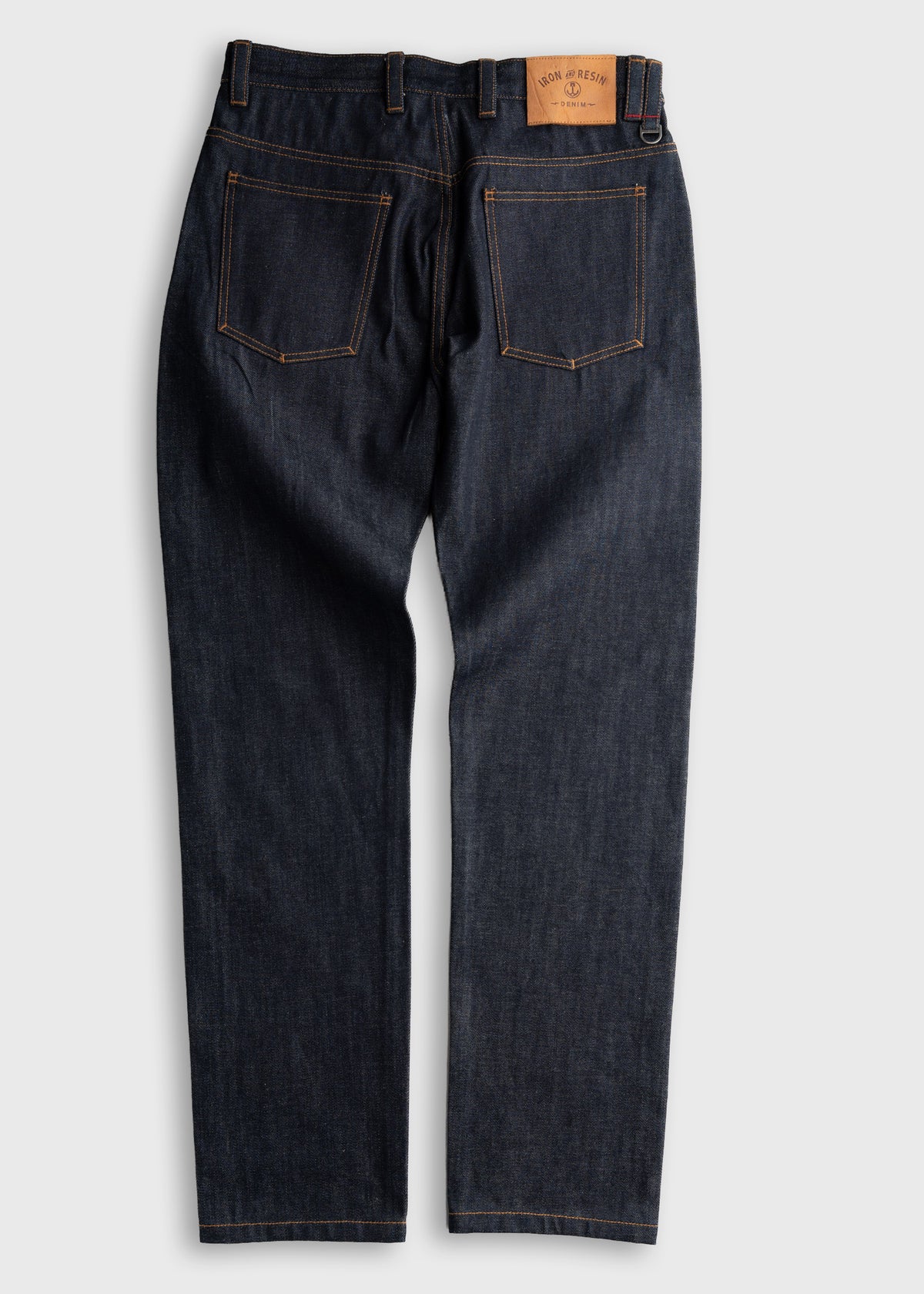 Dark denim jeans with visible orange stitching and a leather patch on the back waistband, displayed on a plain background.